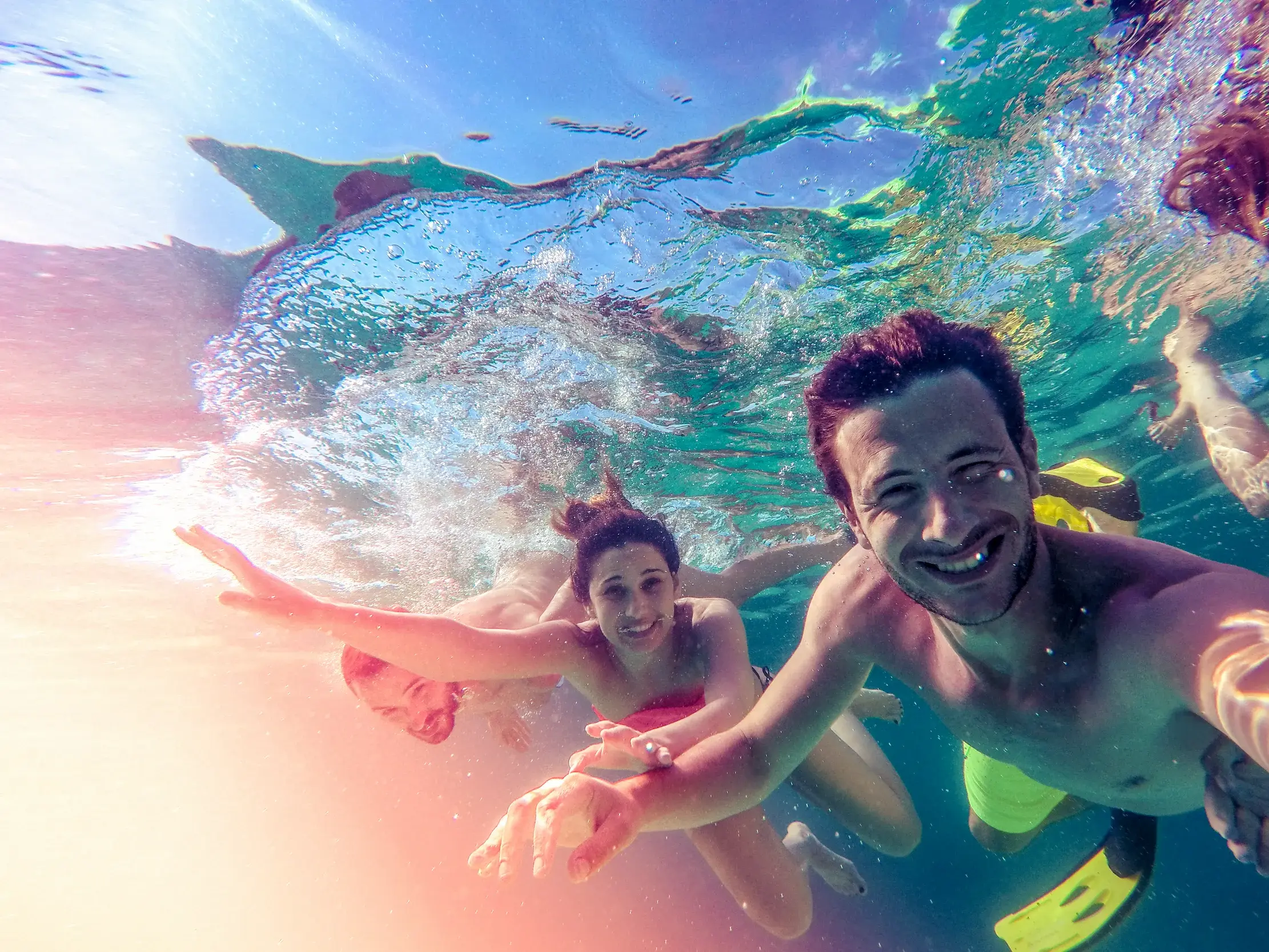Ein junger Mann macht ein fröhliches Unterwasser-Selfie mit seiner Reisegruppe in einer sonnigen Bucht in Griechenland.