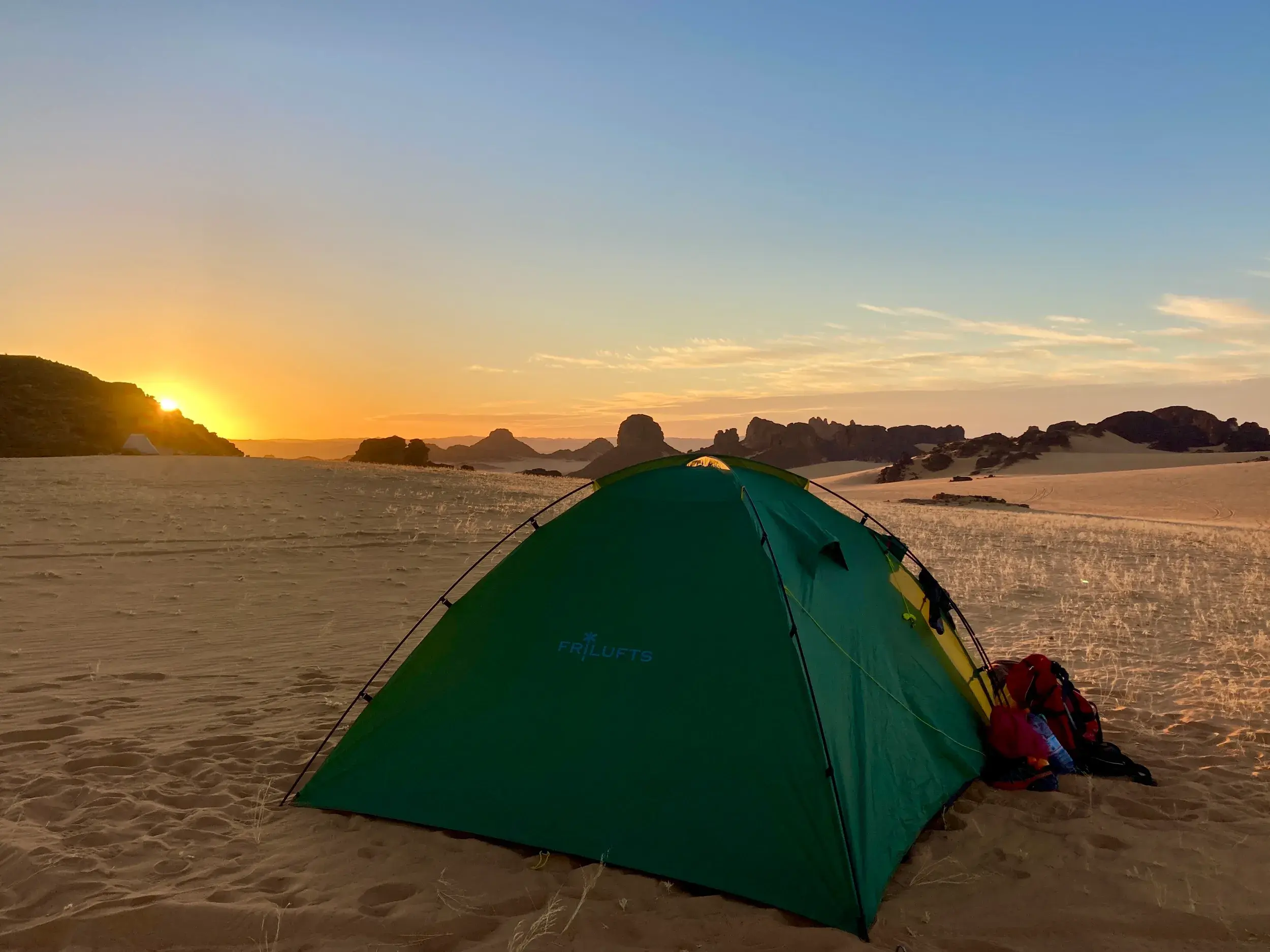 Ein grünes Zelt in der Weite der algerischen Sahara beim Trekking im Tassili n'Ajjer Nationalpark bei Sonnenaufgang.