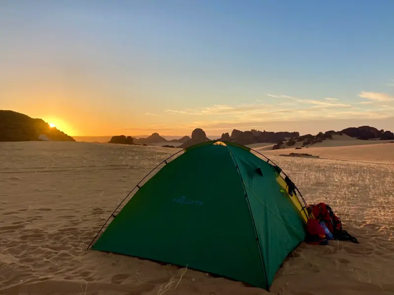 Ein grünes Zelt in der Weite der algerischen Sahara beim Trekking im Tassili n'Ajjer Nationalpark bei Sonnenaufgang.