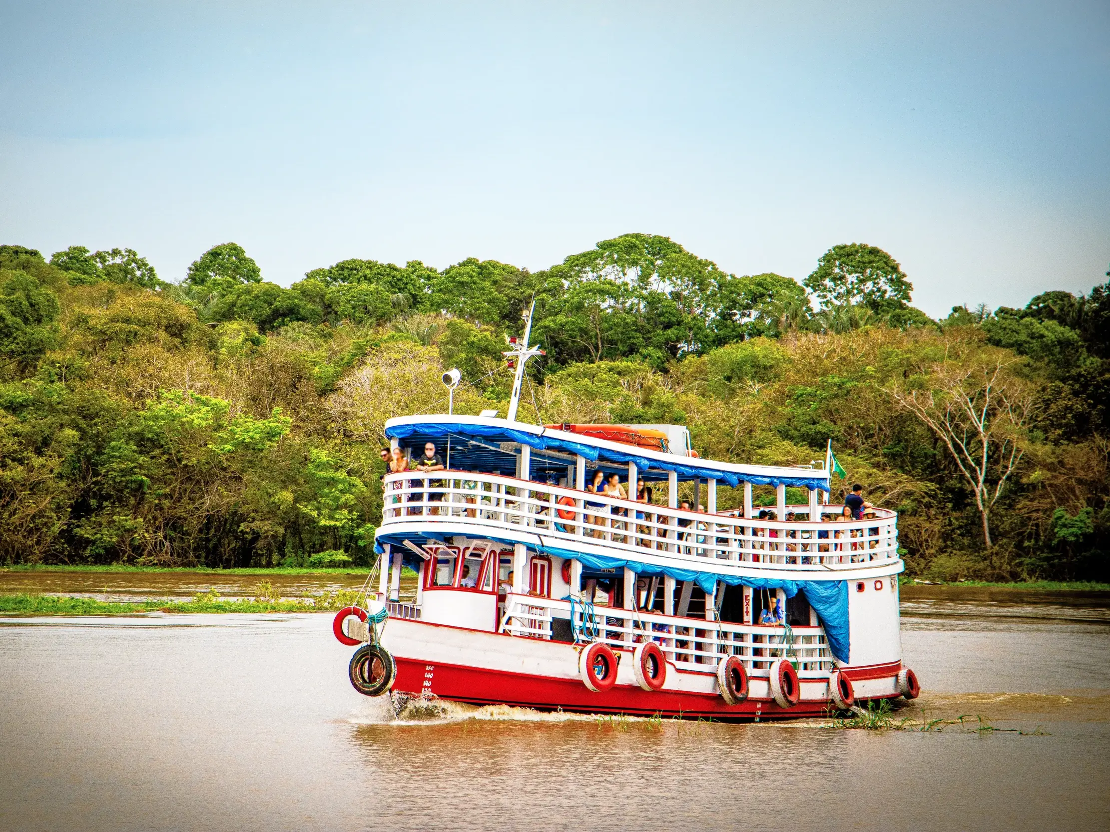 Junge Reisegruppe auf einem typischen Amazonas-Dampfer während einer Bootstour entlang des üppig grünen Regenwaldes Brasiliens.