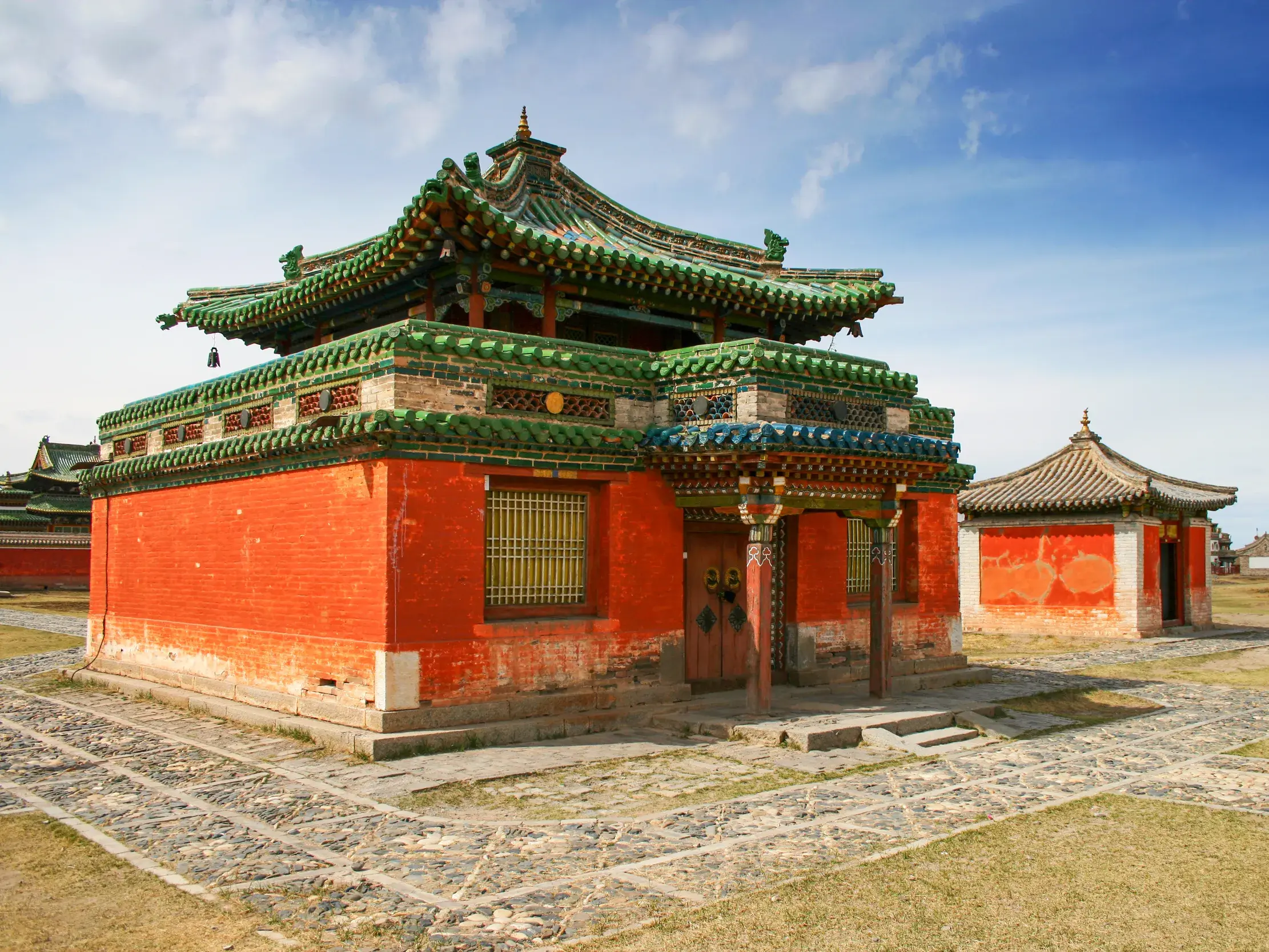 Ein Tempel des Erdene Zuu-Klosters in Karakorum mit roter Fassade und grünem Pagodendach in der mongolischen Steppe.