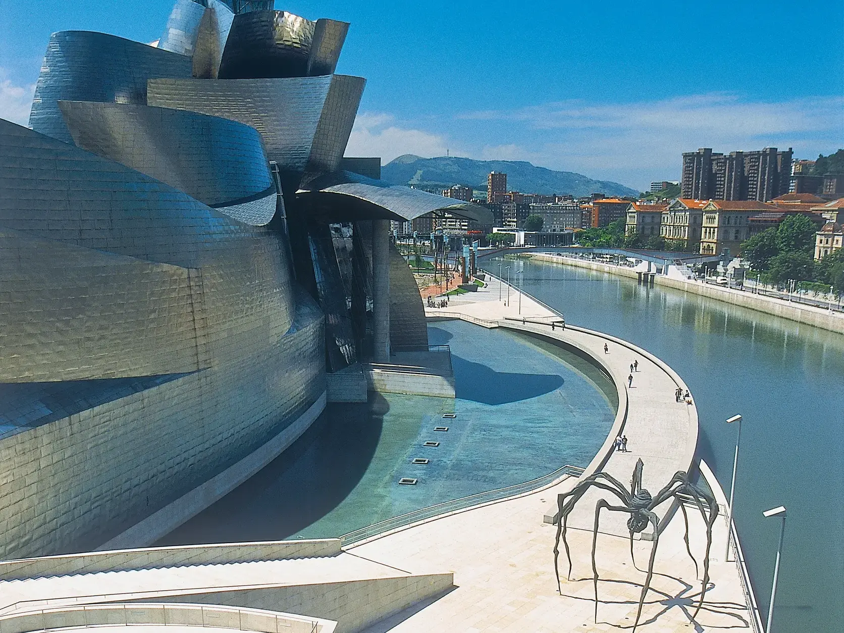 Glänzende Titanfassade des Guggenheim-Museums in Bilbao am Fluss Nervión mit der berühmten Spinnenskulptur Maman.