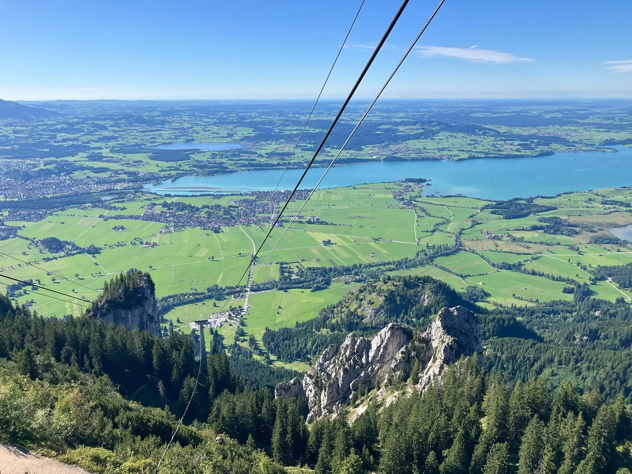 Weitblick von der Tegelbergbahn über bewaldete Felsen der Ammergauer Alpen auf die Seenlandschaft im Füssener Land.