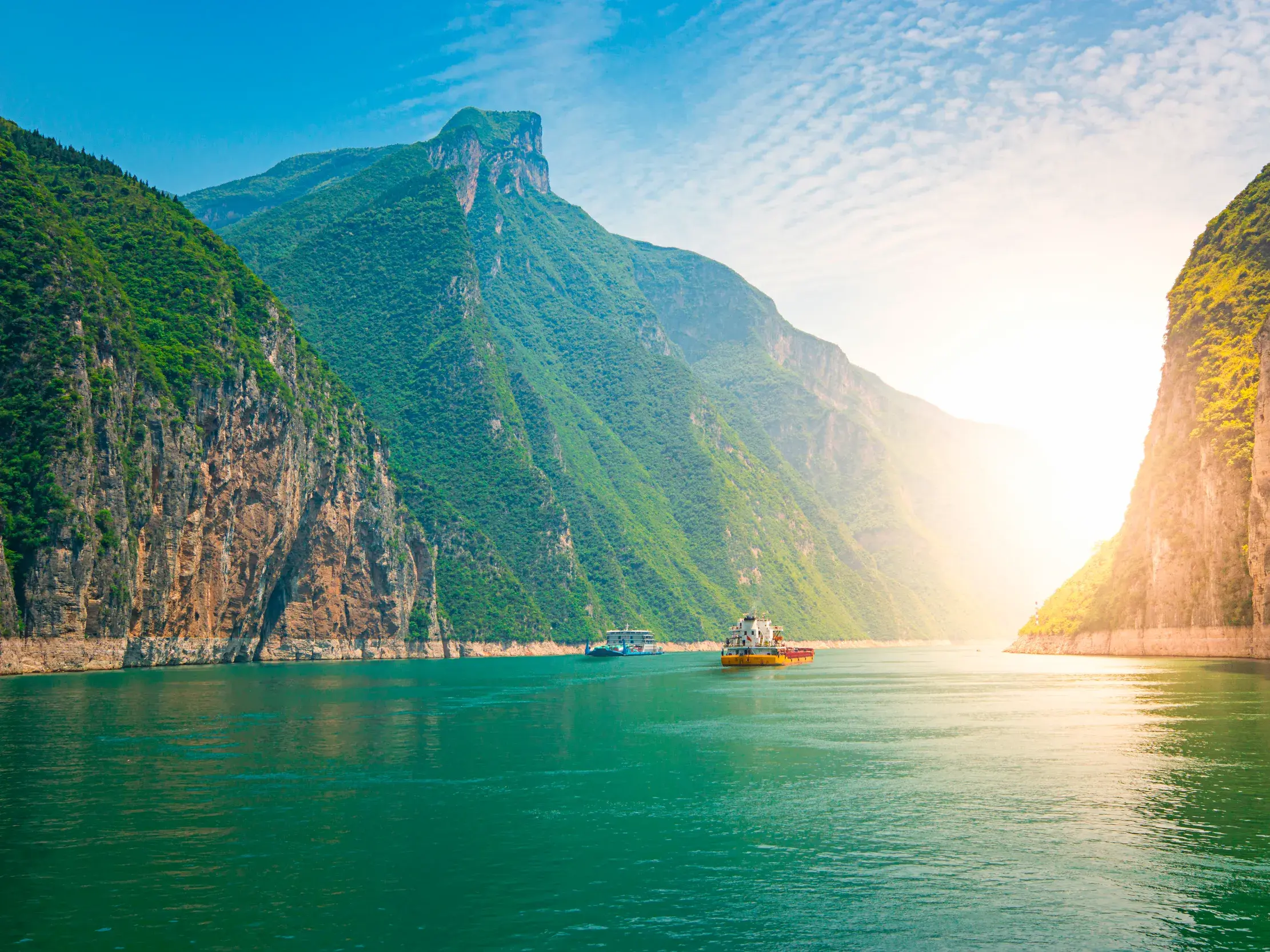 Zwei Schiffe auf dem türkisen Yangze, umgeben von steilen, grünen Felswänden der berühmten Drei Schluchten Chinas.