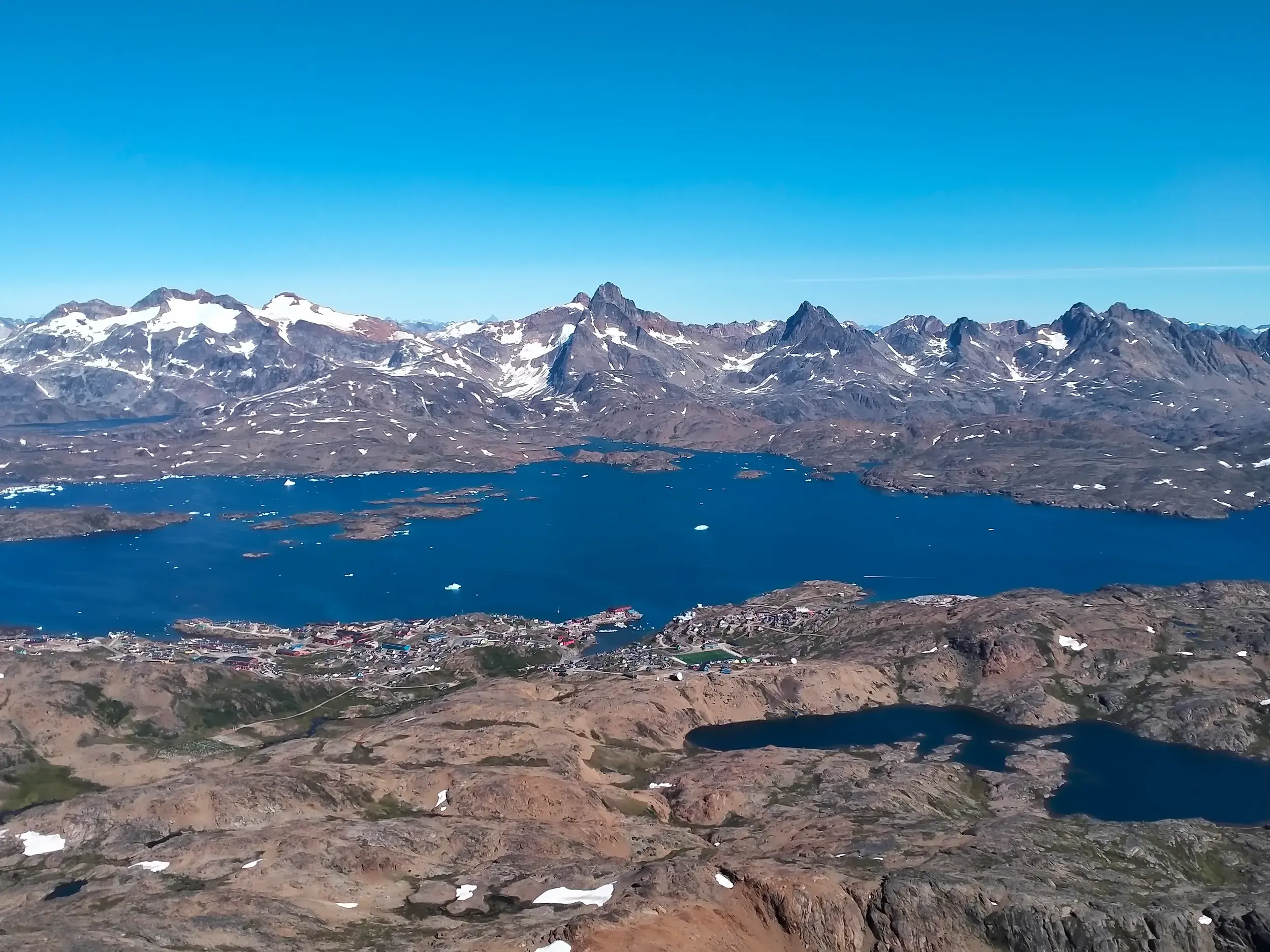 Panoramablick auf die Stadt Tasiilaq am Kong-Oscar-Fjord mit Eisbergen und schneebedeckten Gipfeln in Ostgrönland.