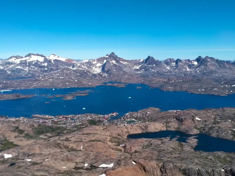 Panoramablick auf die Stadt Tasiilaq am Kong-Oscar-Fjord mit Eisbergen und schneebedeckten Gipfeln in Ostgrönland.