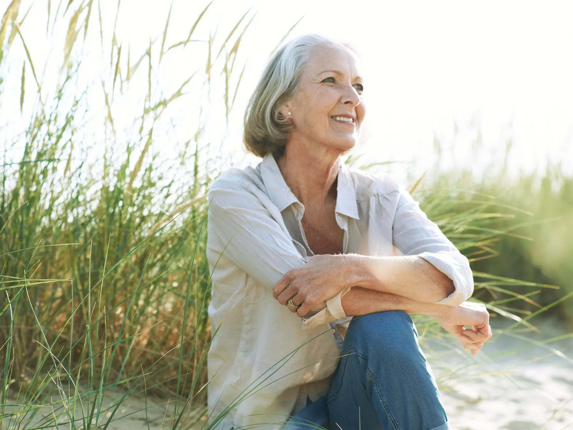 Eine Seniorin genießt auf einer Studiosus Studienreise einen entspannten Moment in den sonnigen Dünen der Ostseeküste.