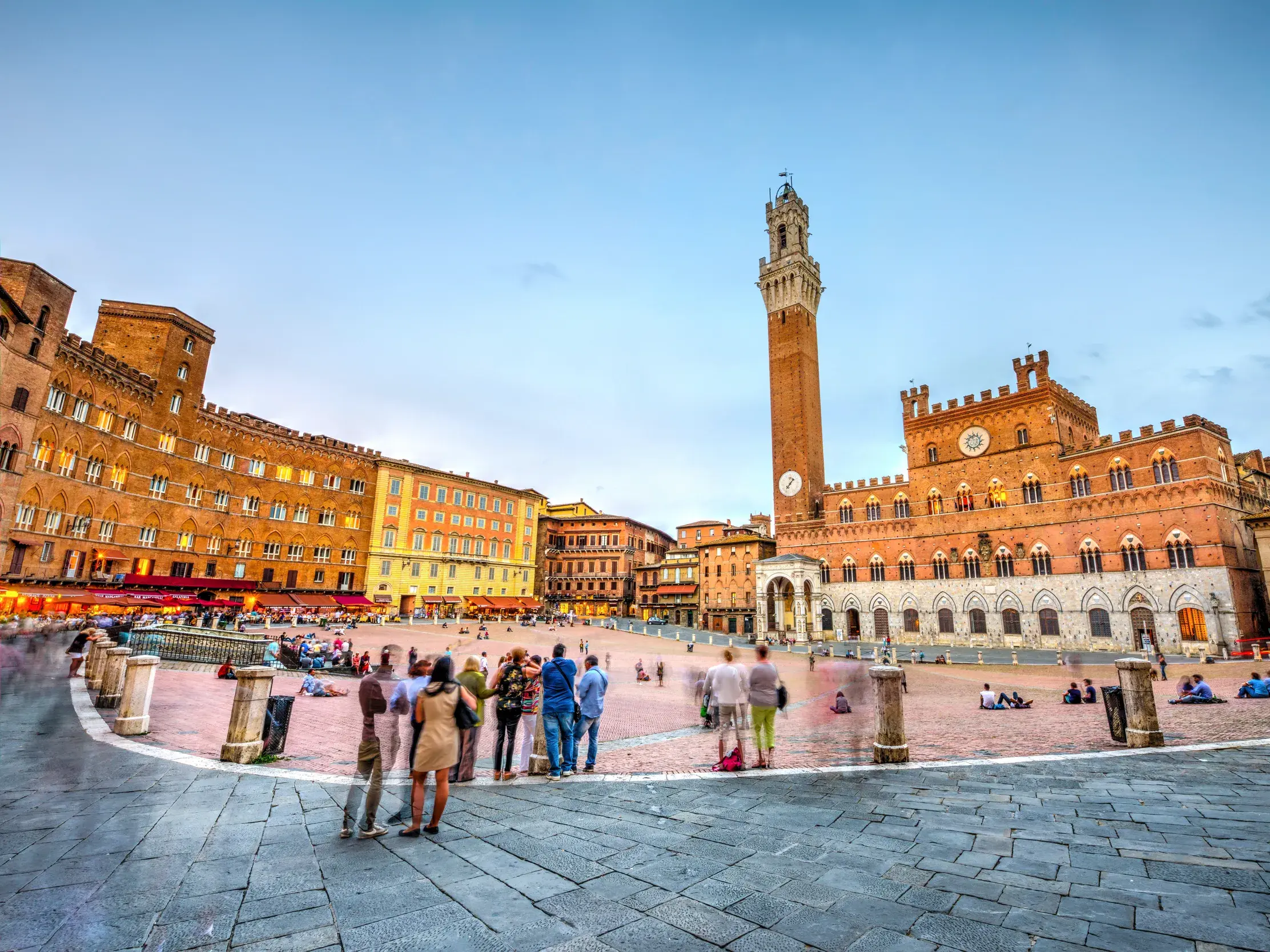 Besucher auf der muschelförmigen Piazza del Campo in Siena vor dem beleuchteten Palazzo Pubblico bei Dämmerung.