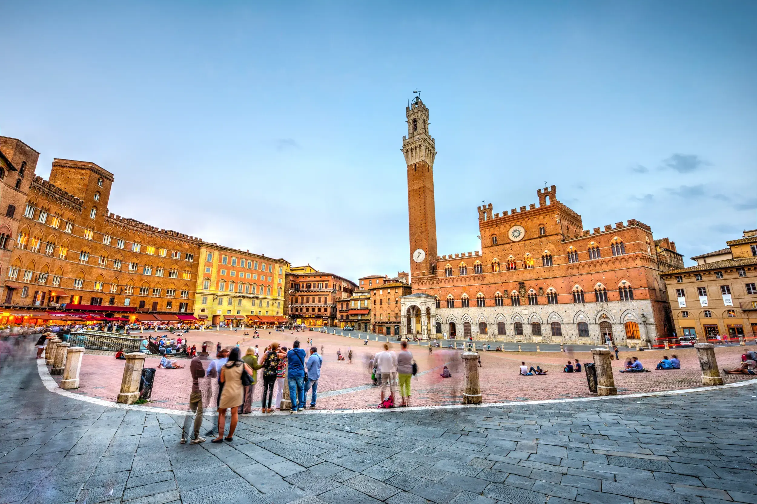 Besucher auf der muschelförmigen Piazza del Campo in Siena vor dem beleuchteten Palazzo Pubblico bei Dämmerung.
