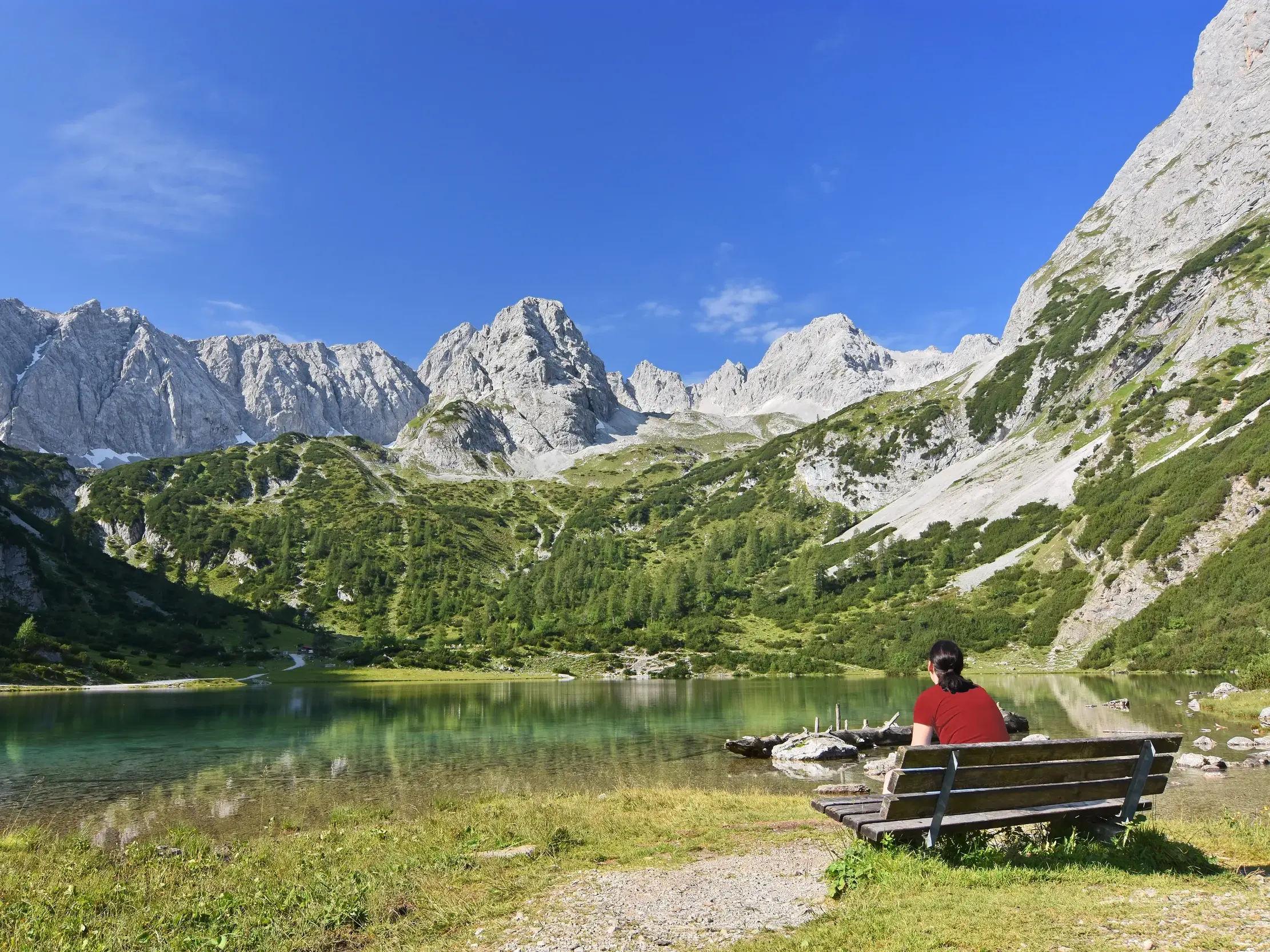 Wanderin bei einer Rast auf einer Bank am Ufer des türkisen Seebensees mit Blick auf die beeindruckenden Alpengipfel.
