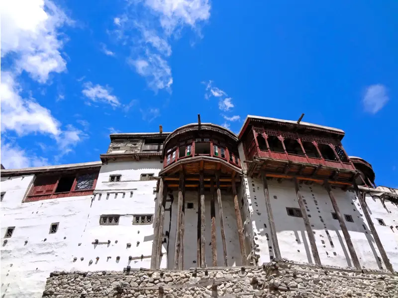 Historisches Baltit Fort im Hunzatal mit weißer Fassade und verzierten Holzbalkonen vor einem strahlend blauen Himmel.