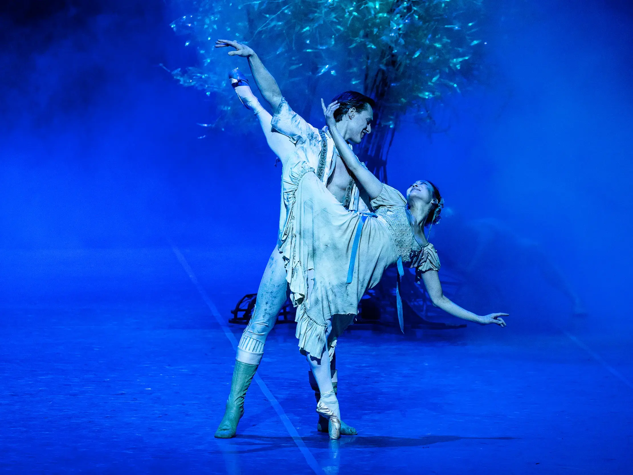 Balletttänzer bei einer anmutigen Hebefigur auf blau beleuchteter Bühne in der Hamburgischen Staatsoper.