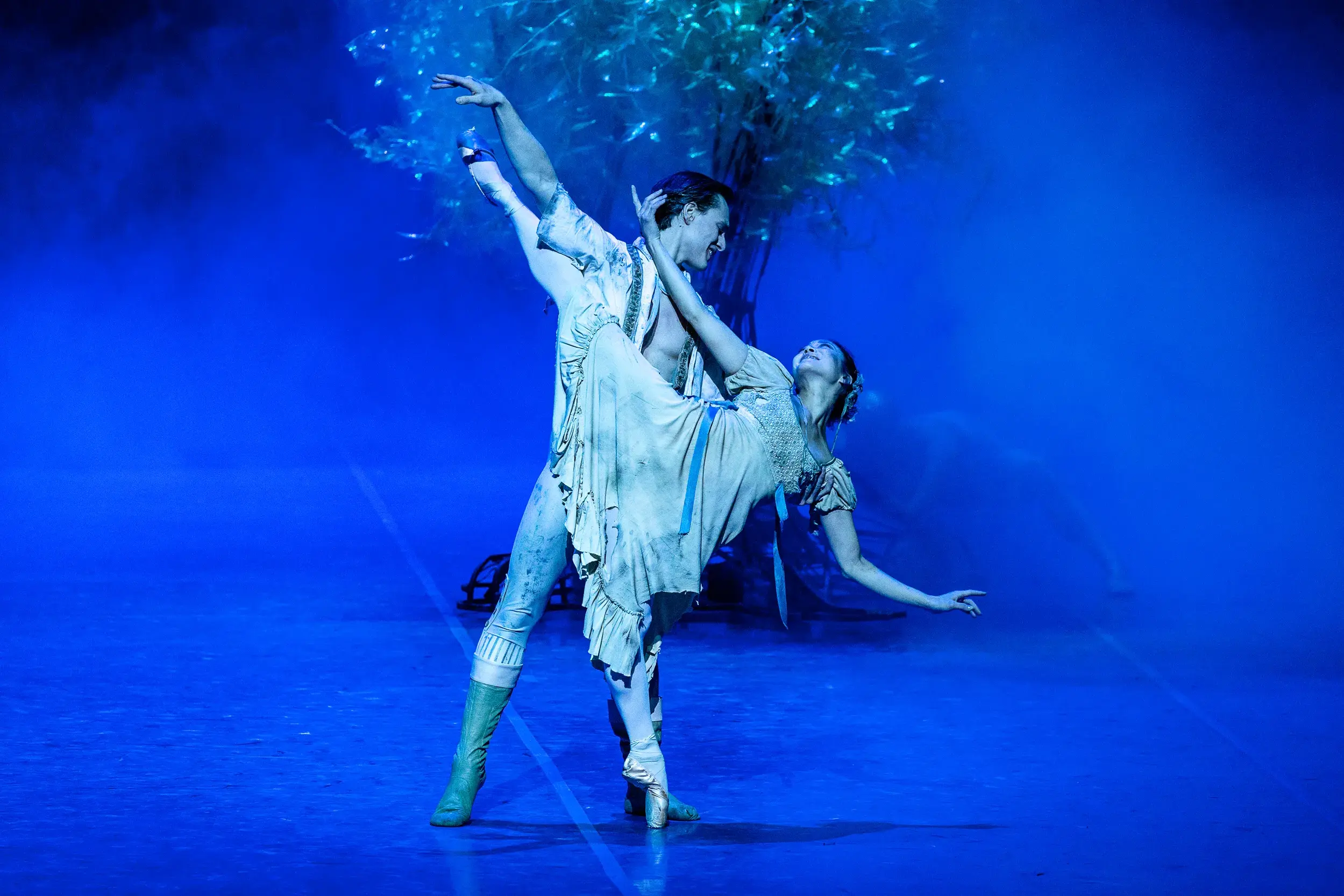 Balletttänzer bei einer anmutigen Hebefigur auf blau beleuchteter Bühne in der Hamburgischen Staatsoper.