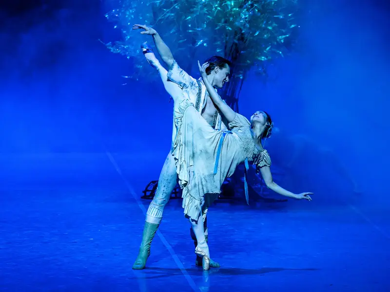 Balletttänzer bei einer anmutigen Hebefigur auf blau beleuchteter Bühne in der Hamburgischen Staatsoper.