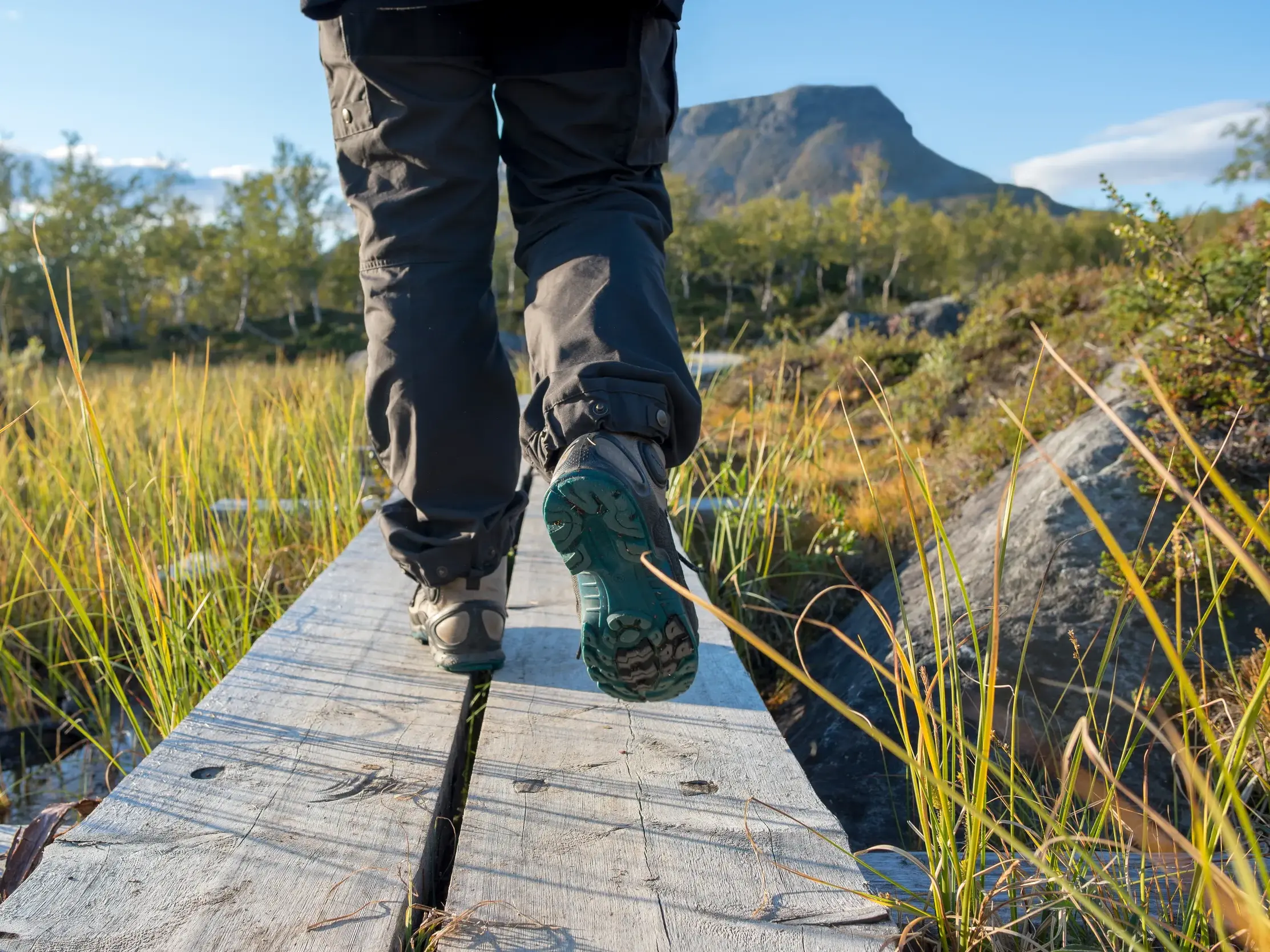 Eine Person wandert auf einem Holzsteg durch die Moorlandschaft des Lemmenjoki-Nationalparks in Finnland.