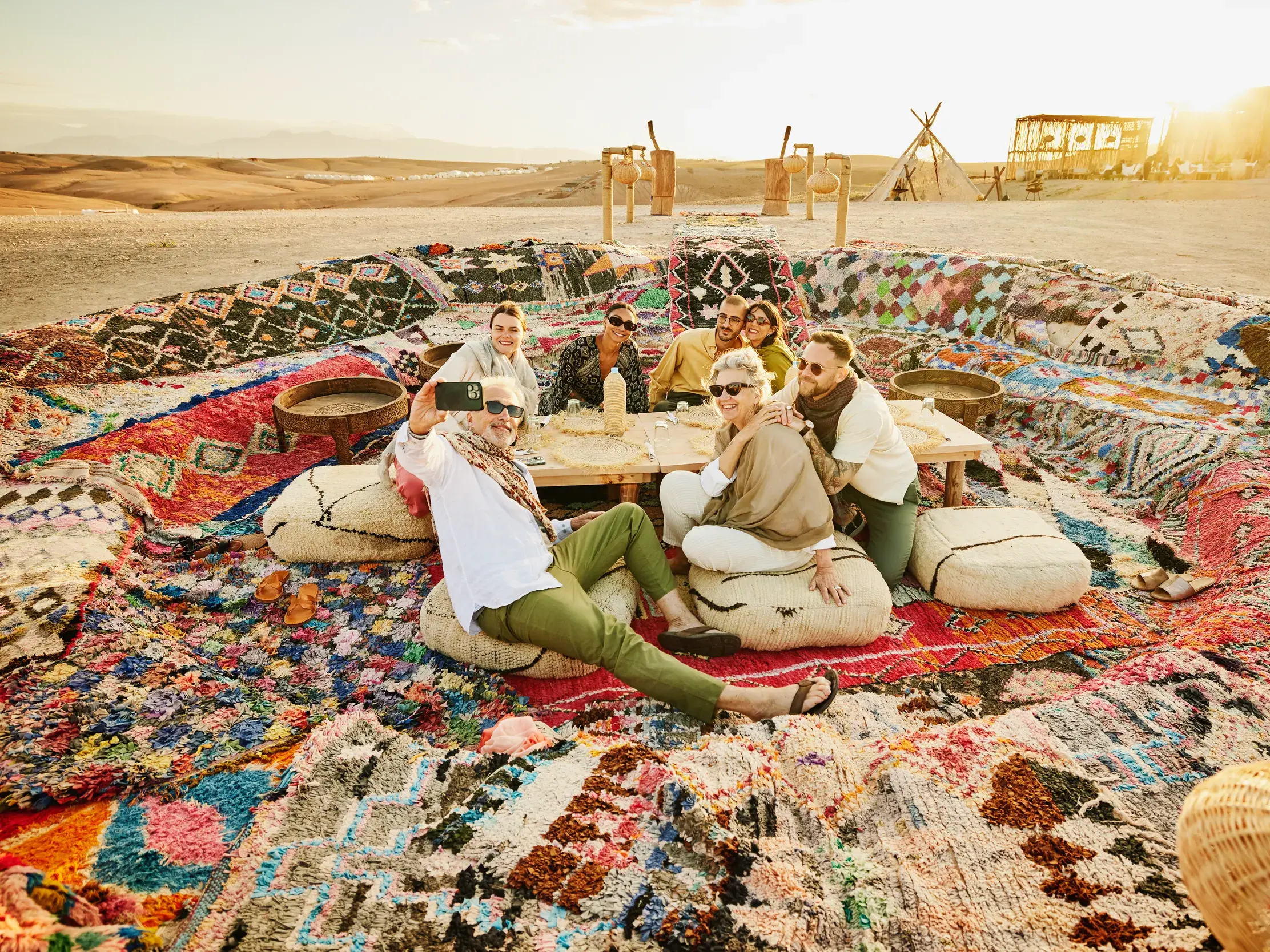 Eine fröhliche Marco Polo Reisegruppe macht ein Selfie bei einem Picknick auf bunten Teppichen in der Wüste Tunesiens.