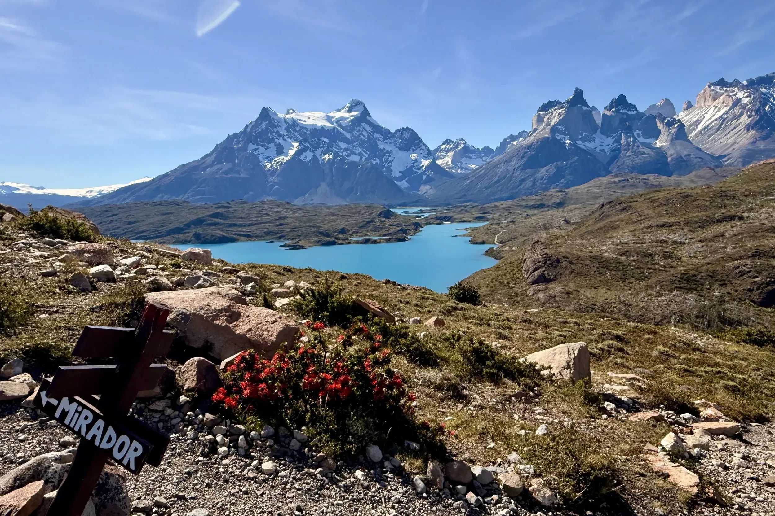 Sonniger Blick vom Mirador Condor auf die Cuernos del Paine und einen türkisen See im Torres del Paine Nationalpark in Patagonien.