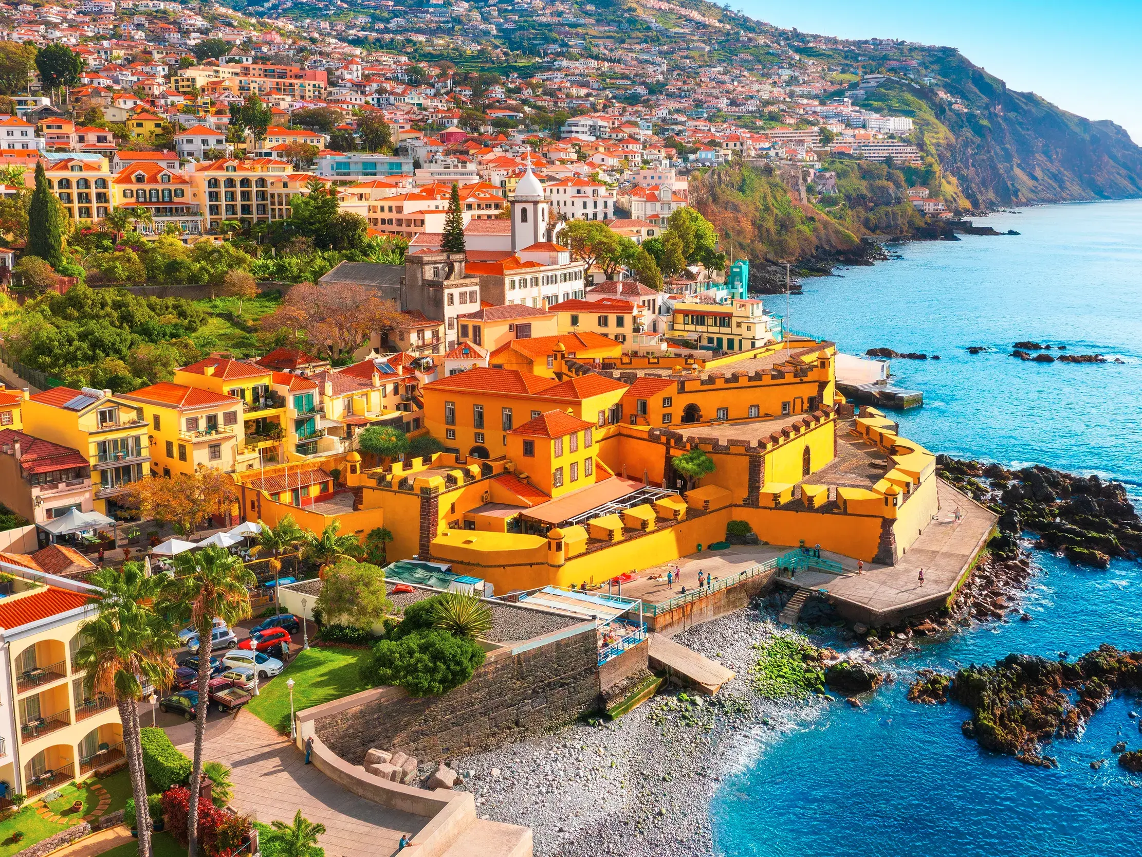 Malerische Küstenansicht von Funchal auf Madeira mit bunten Häusern am Hang und einer gelben Festung am Atlantik.