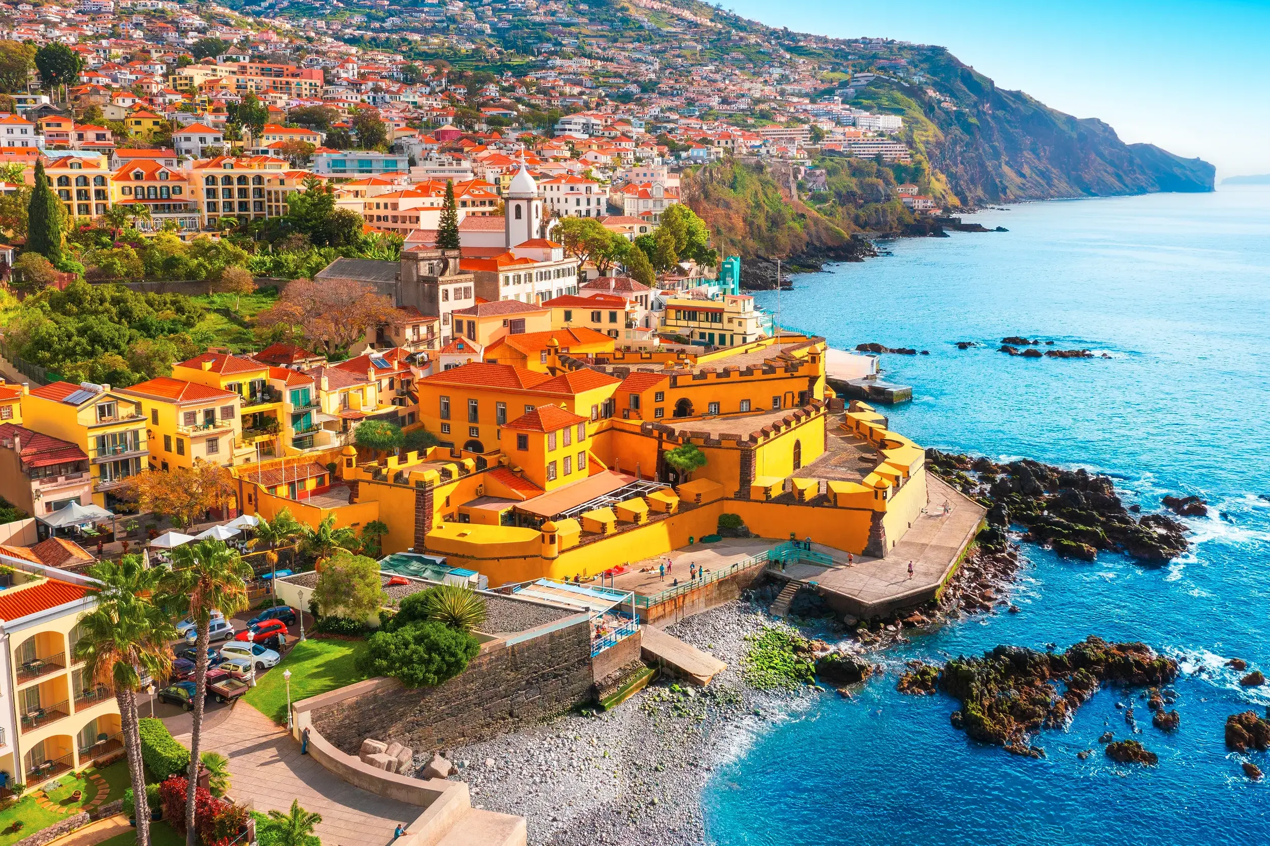 Malerische Küstenansicht von Funchal auf Madeira mit bunten Häusern am Hang und einer gelben Festung am Atlantik.