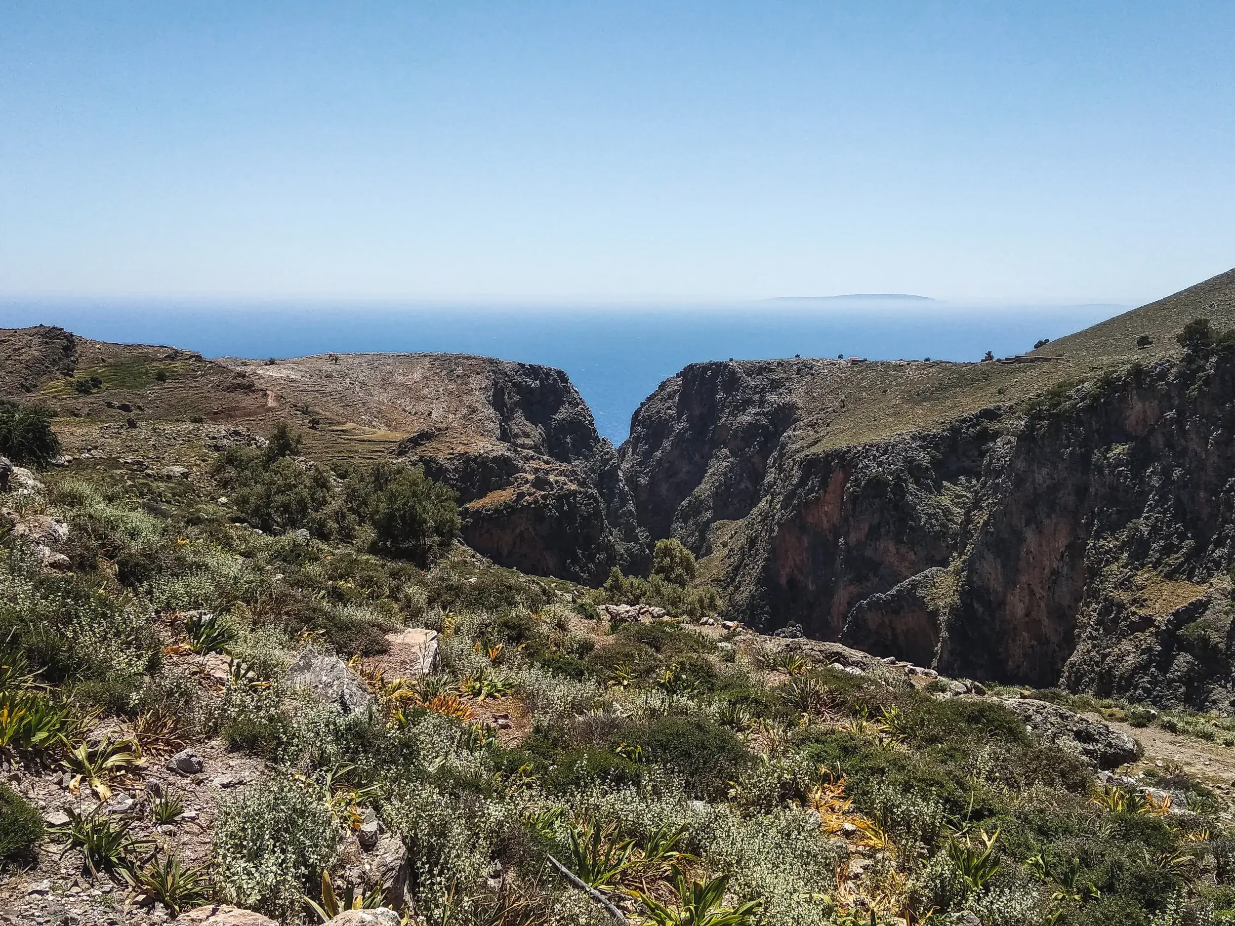 Weitblick von einem Wanderweg über eine tiefe Schlucht in der kargen Berglandschaft von Kreta bis zum Mittelmeer.