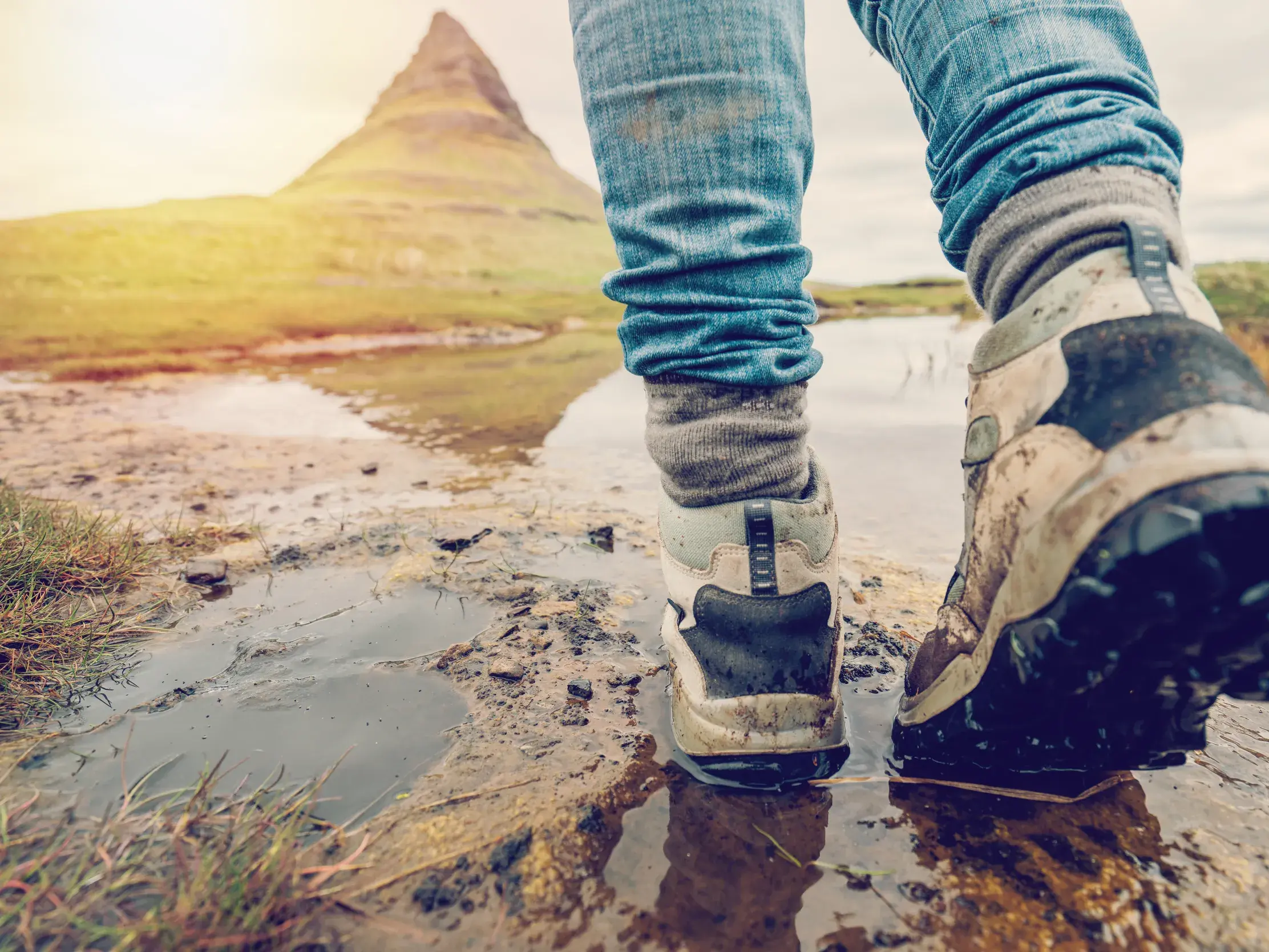 Nahaufnahme der Wanderstiefel einer Person, die auf einem schlammigen Pfad in Island unterwegs ist.