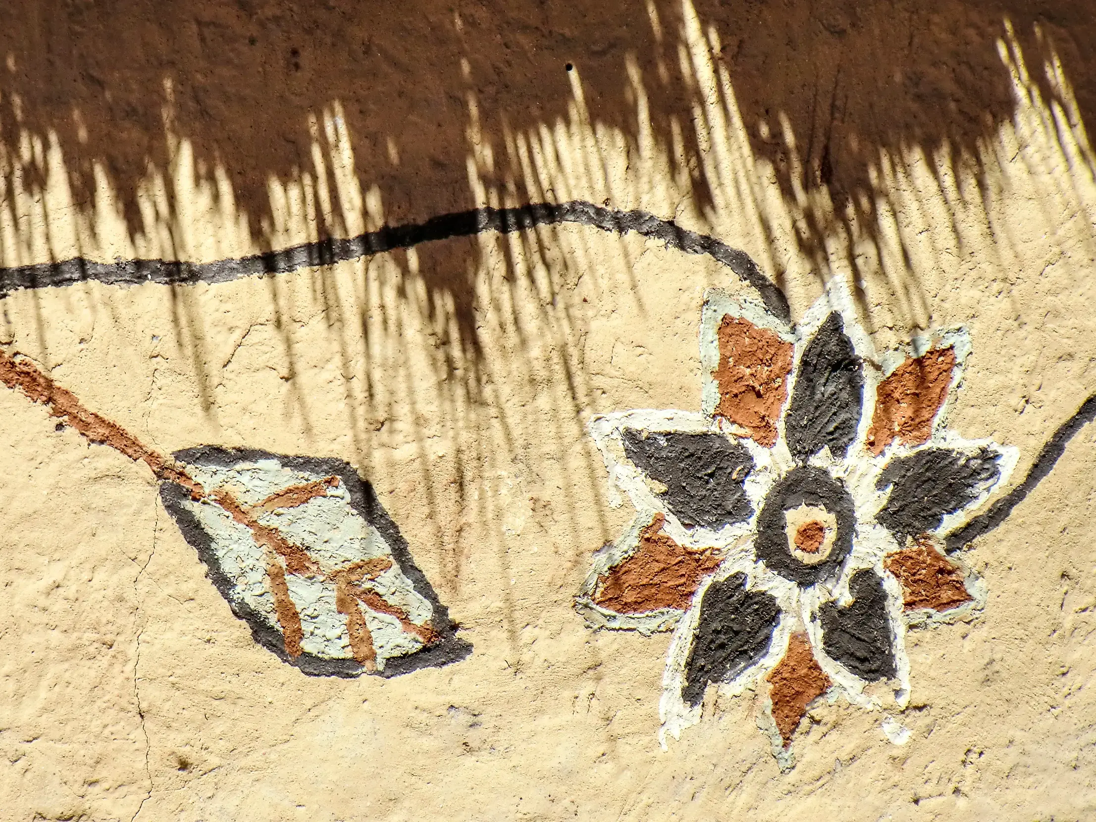 Detail einer traditionellen Wandmalerei mit einer Blume und einem Blatt auf einer rissigen Lehmhütte in der Sonne Namibias.