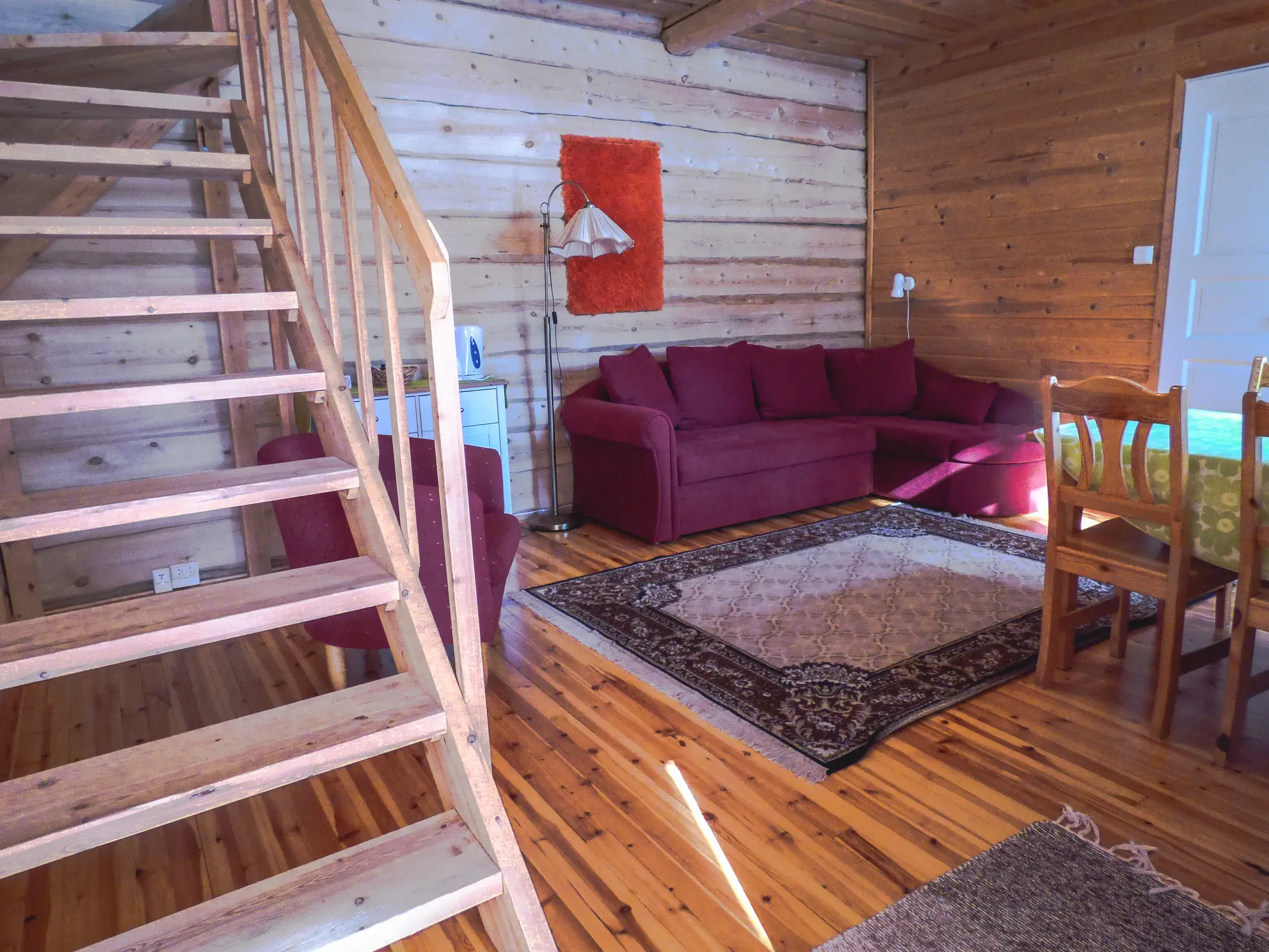 Innenansicht einer finnischen Blockhütte in der Saija Lodge mit Holztreppe, roter Sofaecke und rustikalen Holzwänden.
