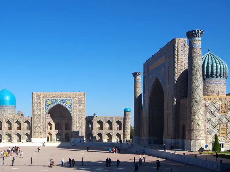 Teilnehmer einer kleinen, geführten Rundreise erkunden die prachtvollen Medresen am sonnigen Registan-Platz in Samarkand.