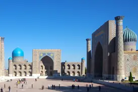 Teilnehmer einer kleinen, geführten Rundreise erkunden die prachtvollen Medresen am sonnigen Registan-Platz in Samarkand.