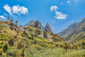 Sonniger Blick in das grüne Tal von Benchijigua auf La Gomera mit Palmen, Häusern am Hang und markanten Vulkanfelsen.