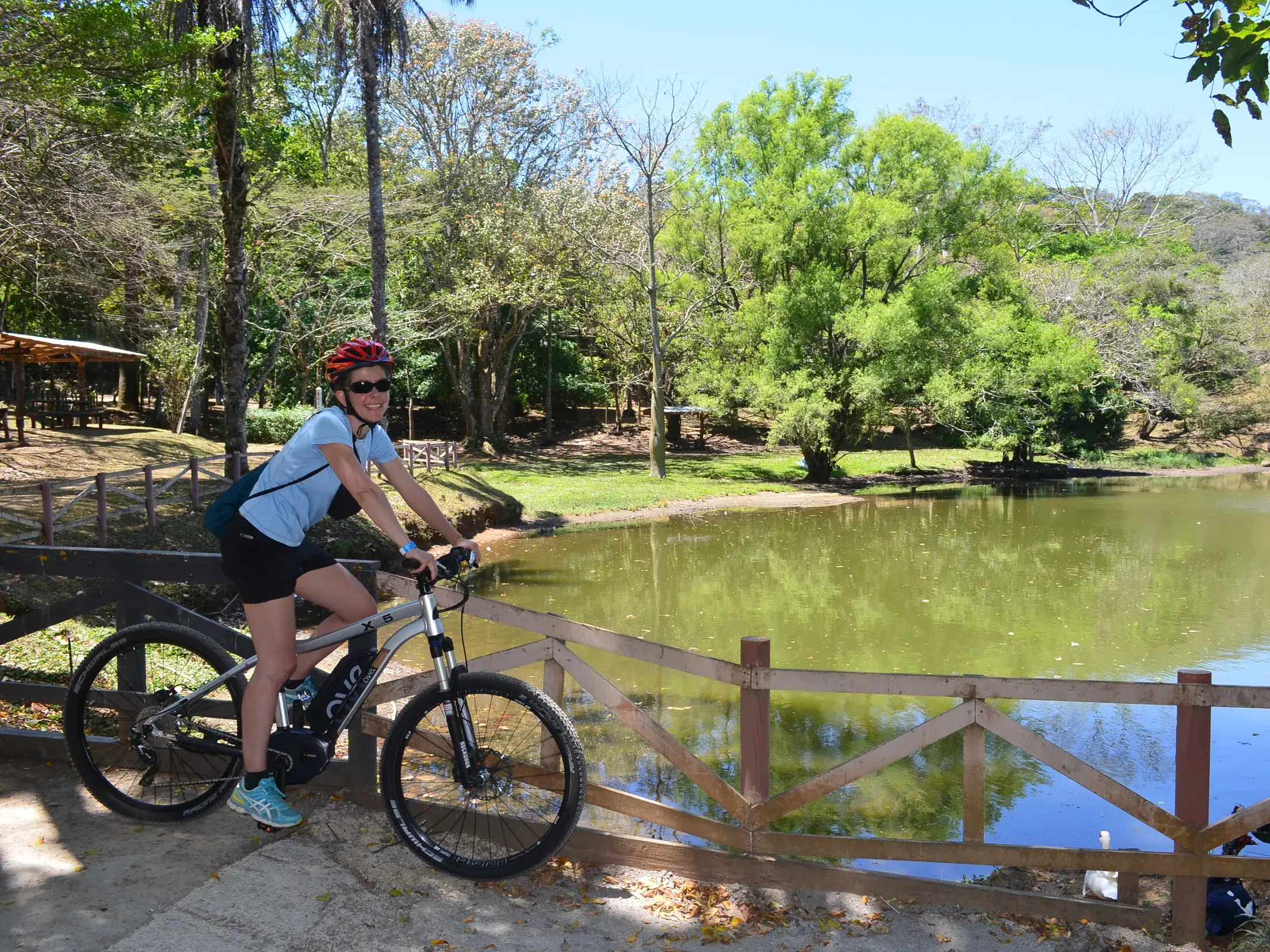 Eine Teilnehmerin einer geführten Radreise in Costa Rica hält mit ihrem Mountainbike an einem idyllischen, grünen See.