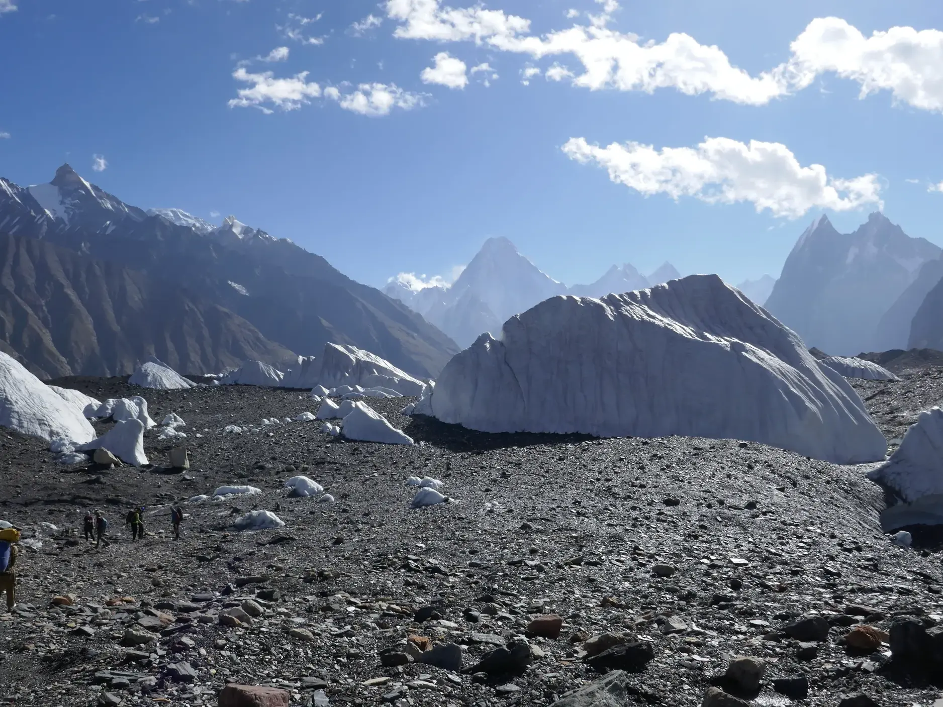 Eine Trekkinggruppe mit Trägern wandert über den schuttbedeckten Baltoro-Gletscher vor der Bergkulisse des Karakorum.