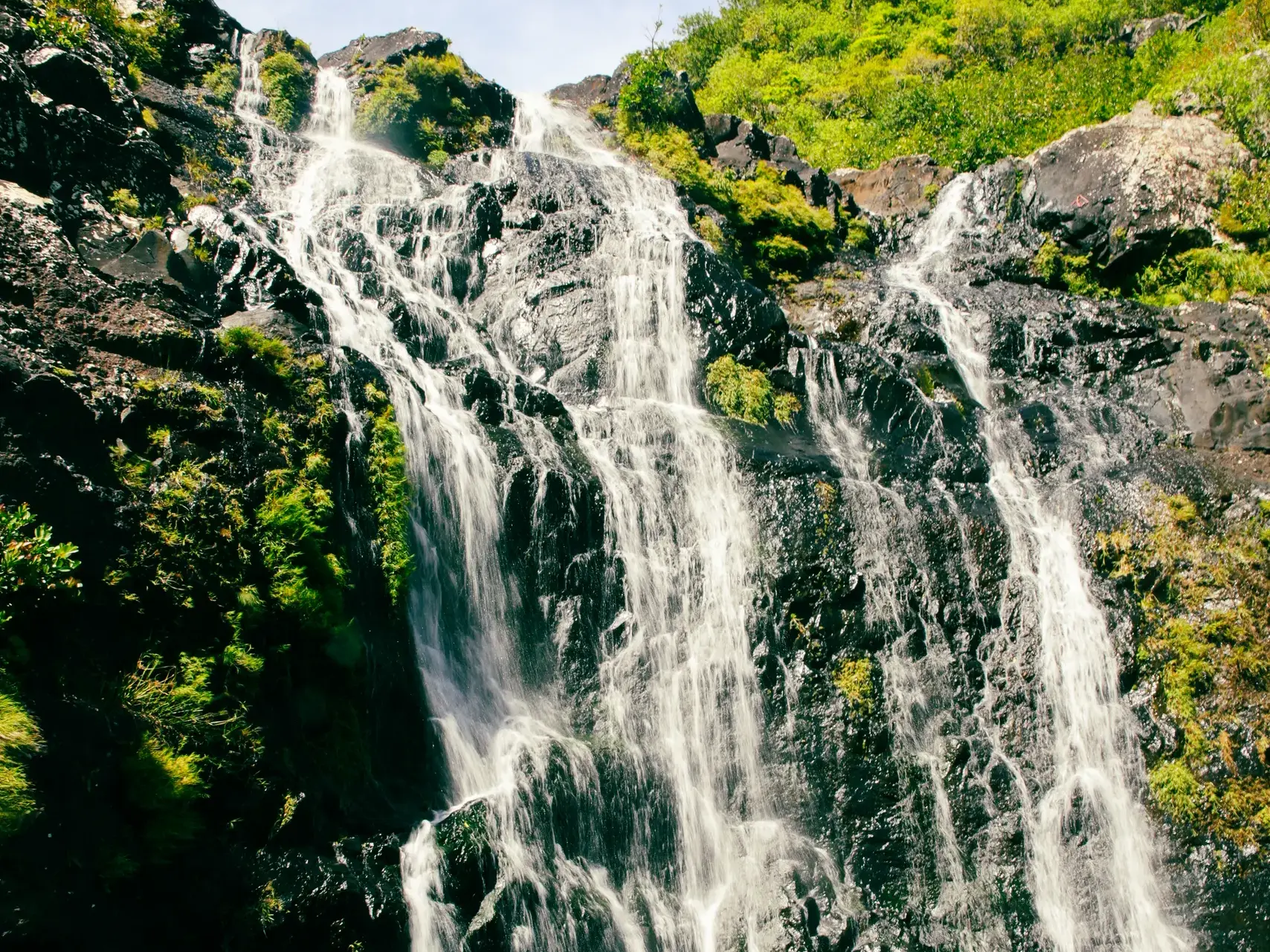 Nahaufnahme der Tamarind-Fälle auf Mauritius, deren Wasser in zahlreichen Kaskaden über dunkle, mit üppig grünen Pflanzen bewachsene Felsen stürzt.