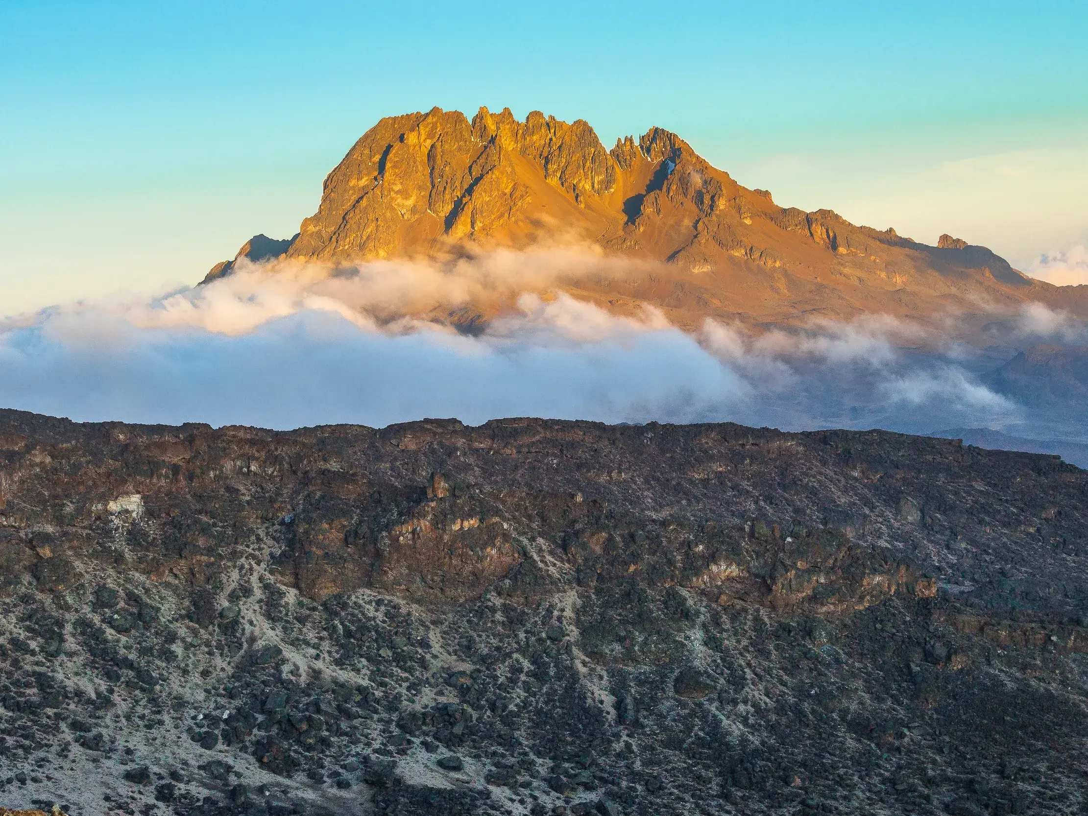 Goldener Sonnenaufgang am Mawenzi-Gipfel auf der Kikelewa-Route am Kilimanjaro, über einer kargen Vulkanlandschaft.