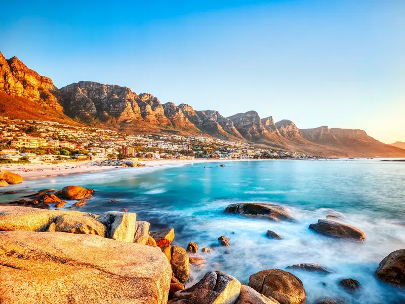 Goldener Sonnenuntergang an der Felsenküste von Camps Bay mit Blick auf die Bergkette der Zwölf Apostel in Kapstadt.
