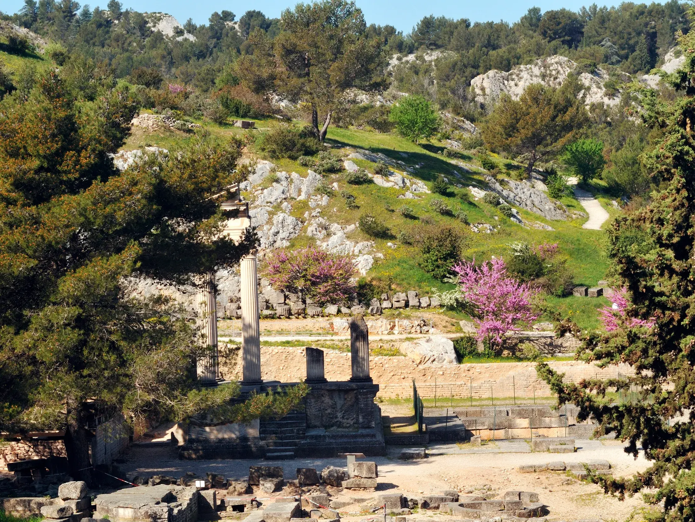 Antike Ruinen der römischen Ausgrabungsstätte Glanum bei Saint-Rémy-de-Provence, umgeben von den grünen Hügeln der Alpilles.