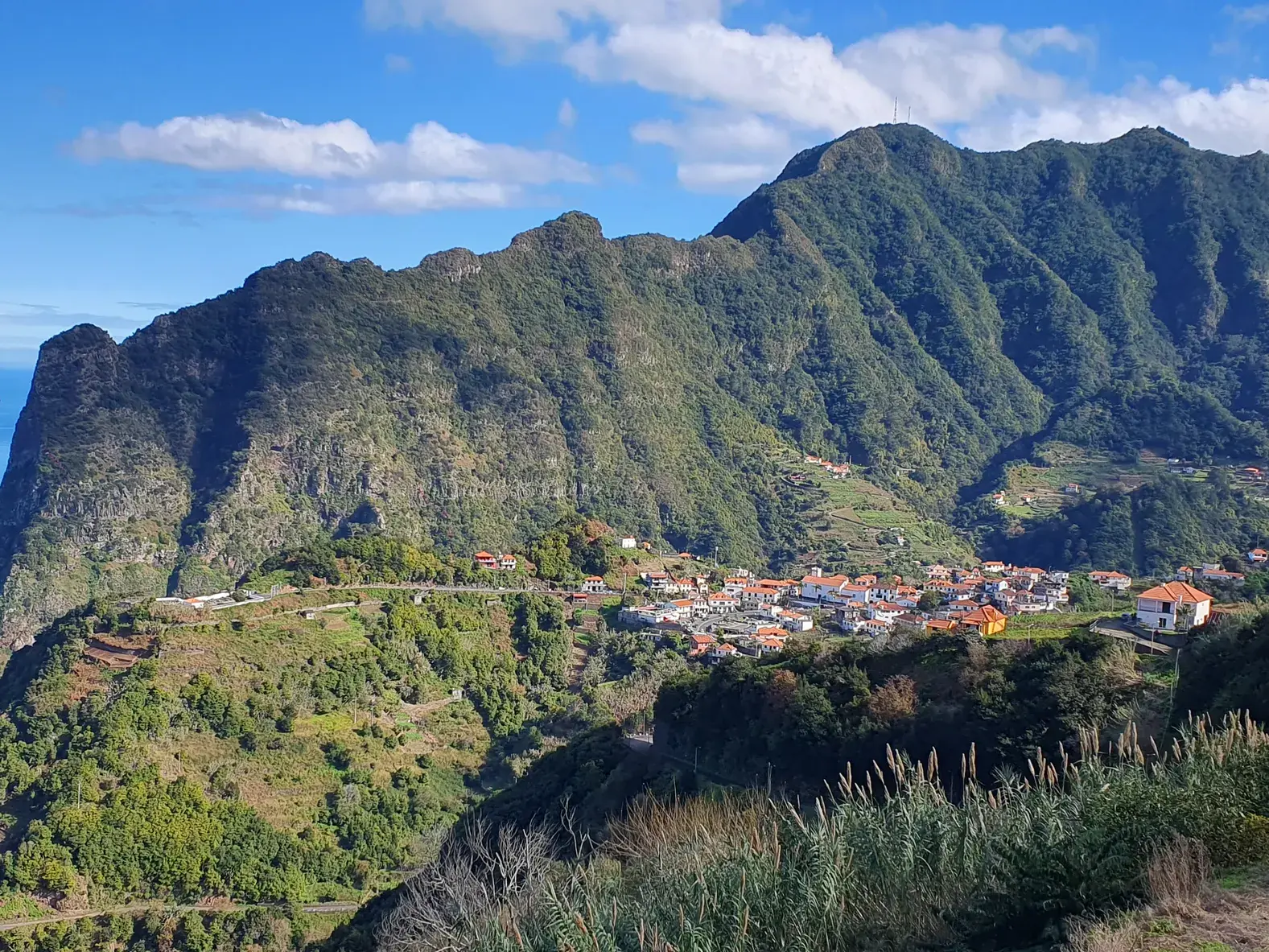 Panoramablick auf das Dorf Curral das Freiras im tiefen Nonnental, umgeben von steilen, grünen Bergen auf einer Wanderreise auf Madeira.