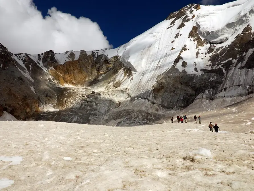 Hauser-Trekkinggruppe auf einem weiten Schneefeld vor der gewaltigen, vergletscherten Diamir-Flanke des Nanga Parbat in Pakistan.