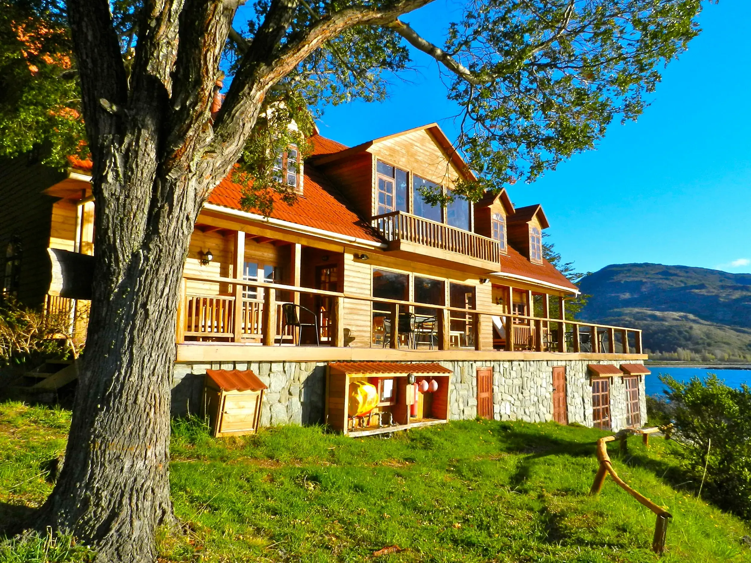 Sonnige Außenansicht der rustikalen Terra Luna Lodge am Ufer des Lago General Carrera mit Blick auf die Berge Patagoniens.