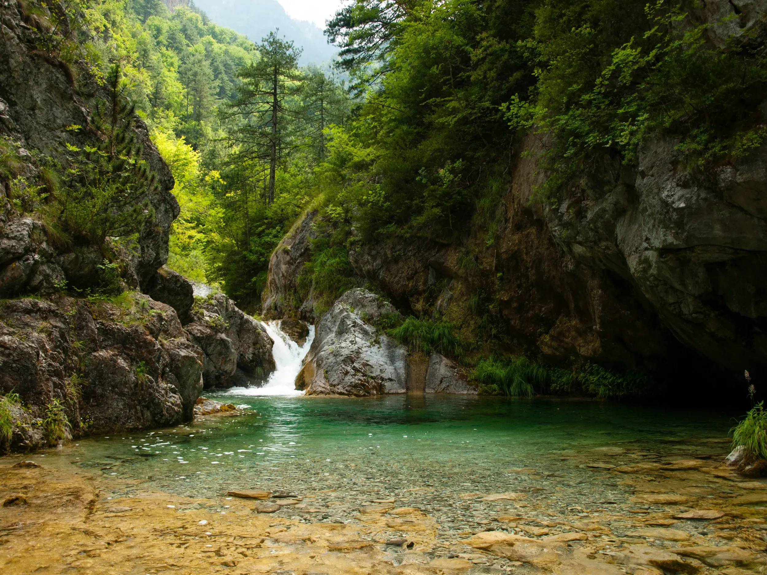 Ein kleiner Wasserfall plätschert in einen türkisfarbenen, klaren Gumpen in der felsigen Enipeas-Schlucht im Olymp-Massiv.