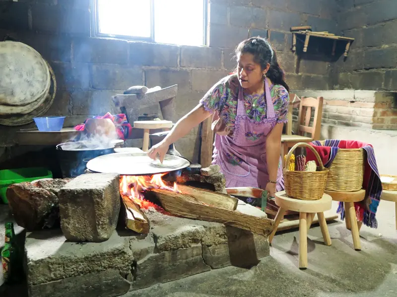 Eine einheimische Frau in Mexiko bereitet in einer rustikalen Steinküche traditionelle Tortillas über einem offenen Feuer zu.