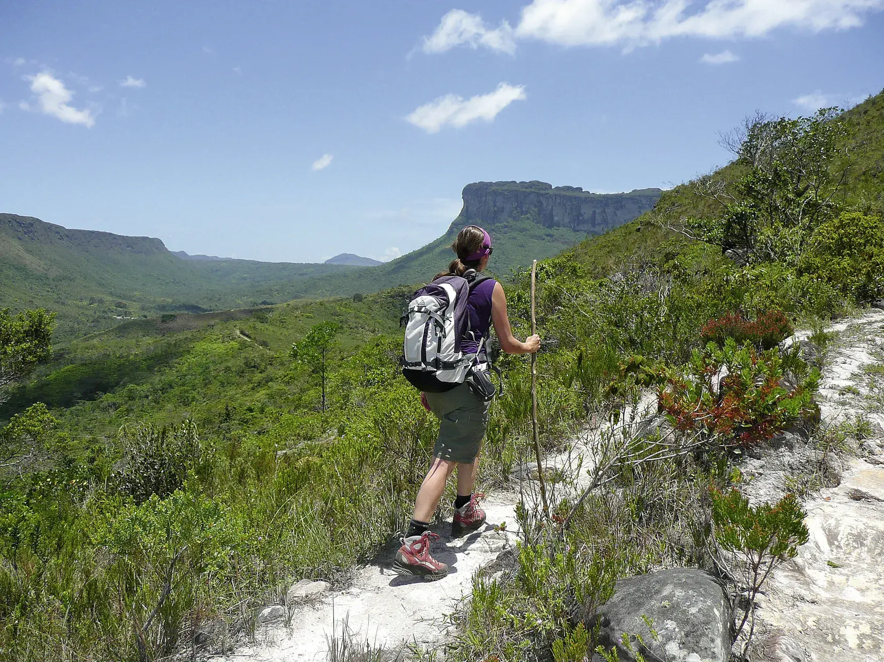 Eine Wanderin mit Rucksack und Stock blickt beim Trekking über die grünen Täler des Chapada Diamantina Nationalparks.