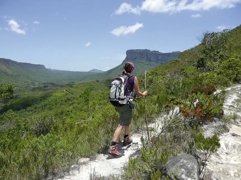 Eine Wanderin mit Rucksack und Stock blickt beim Trekking über die grünen Täler des Chapada Diamantina Nationalparks.