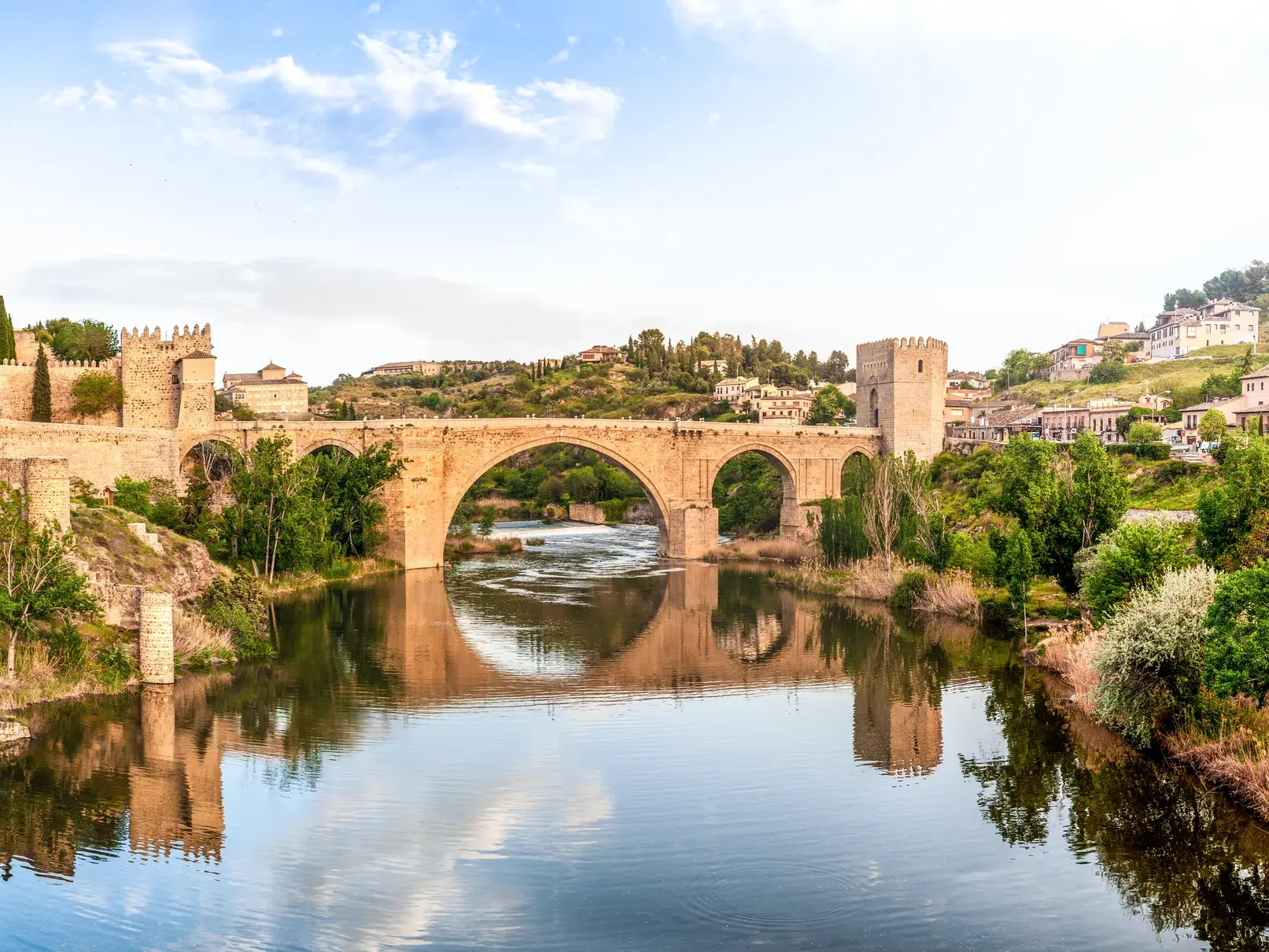 Die historische Steinbrücke von Toledo mit ihren Wehrtürmen spiegelt sich malerisch im ruhigen Wasser des Río Tajo.