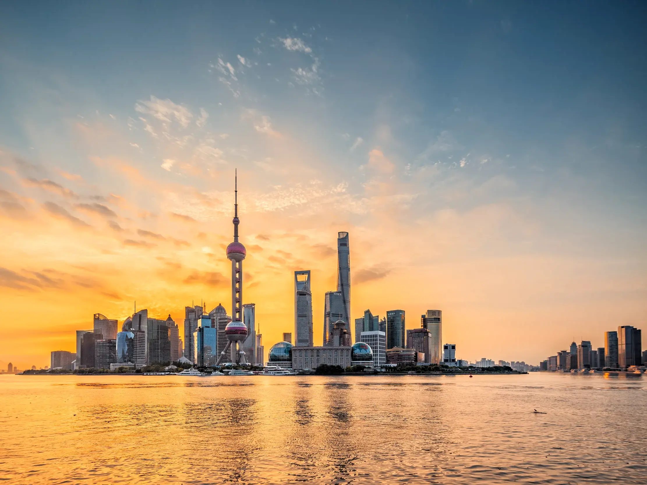 Die Skyline von Shanghai mit dem Oriental Pearl Tower und Wolkenkratzern im goldenen Licht des Sonnenuntergangs am Huangpu-Fluss.