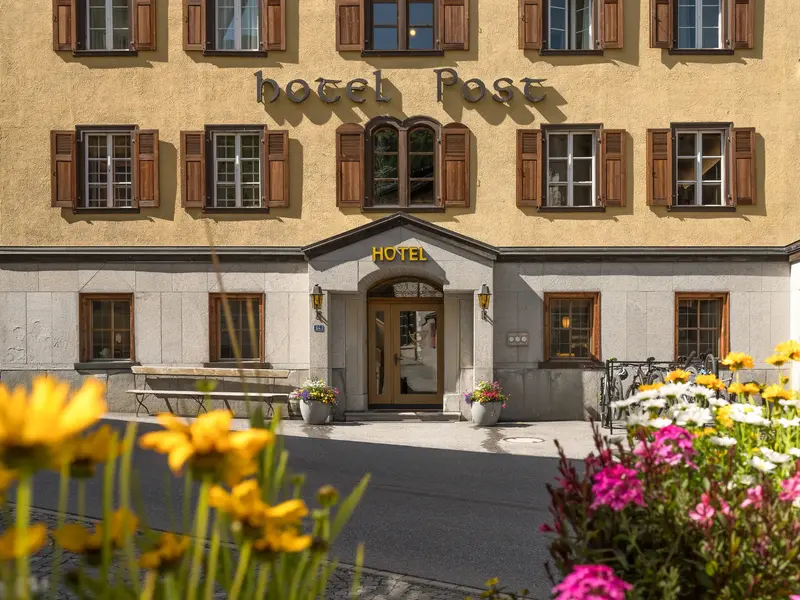 Traditionelle Fassade des Komforthotels in Bivio, Graubünden, mit Holzläden und farbenfrohen Blumen am Eingang.