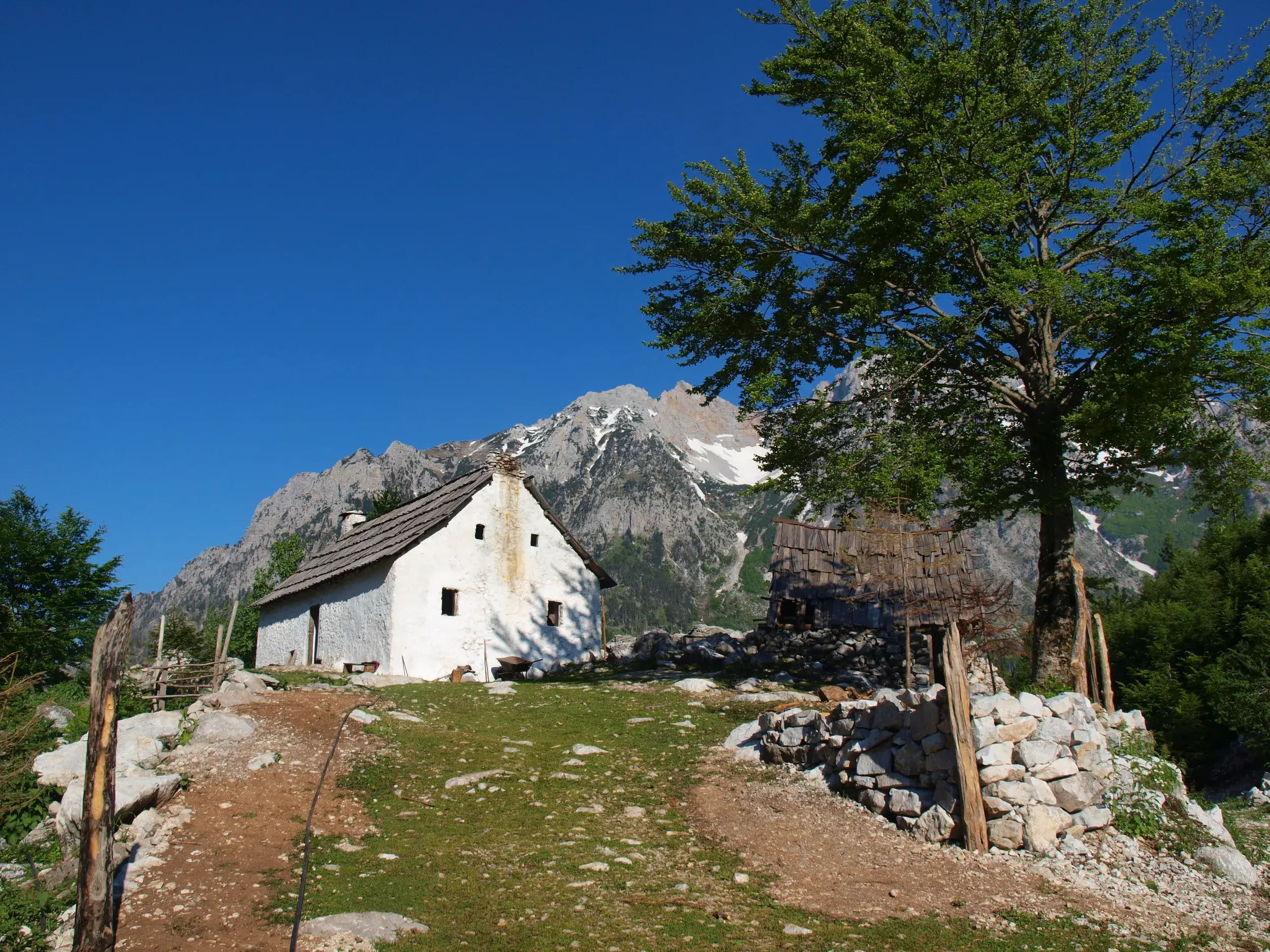 Rustikale Steinhütte auf einer Alm im Valbona-Nationalpark mit Blick auf die majestätischen Gipfel der Albanischen Alpen.