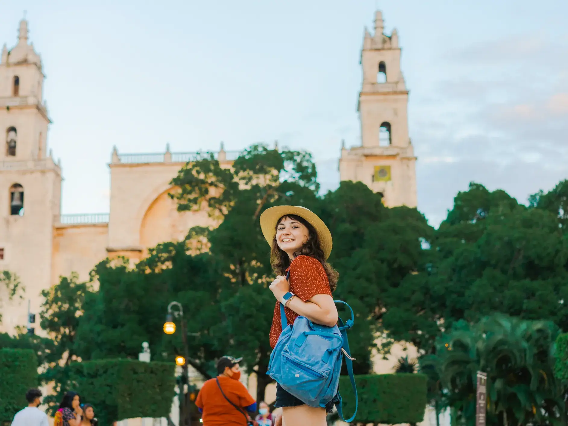 Eine junge Reisende mit Hut und Rucksack erkundet lächelnd die Kolonialstadt Valladolid vor der Kathedrale San Servacio.