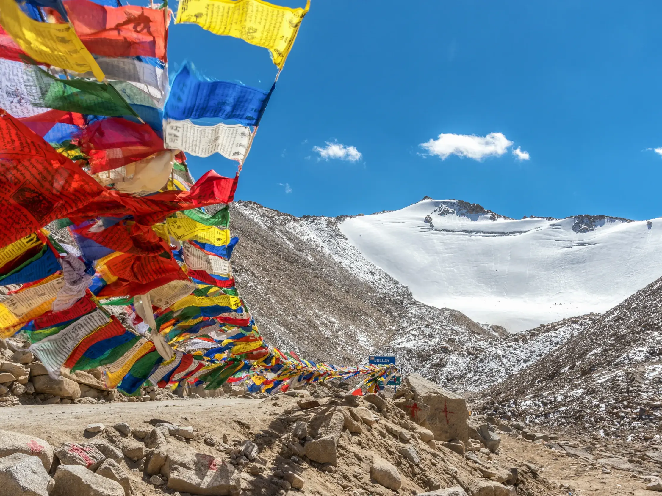 Bunte tibetische Gebetsfahnen wehen im Wind am Khardung La vor einem schneebedeckten Gipfel im Himalaya.