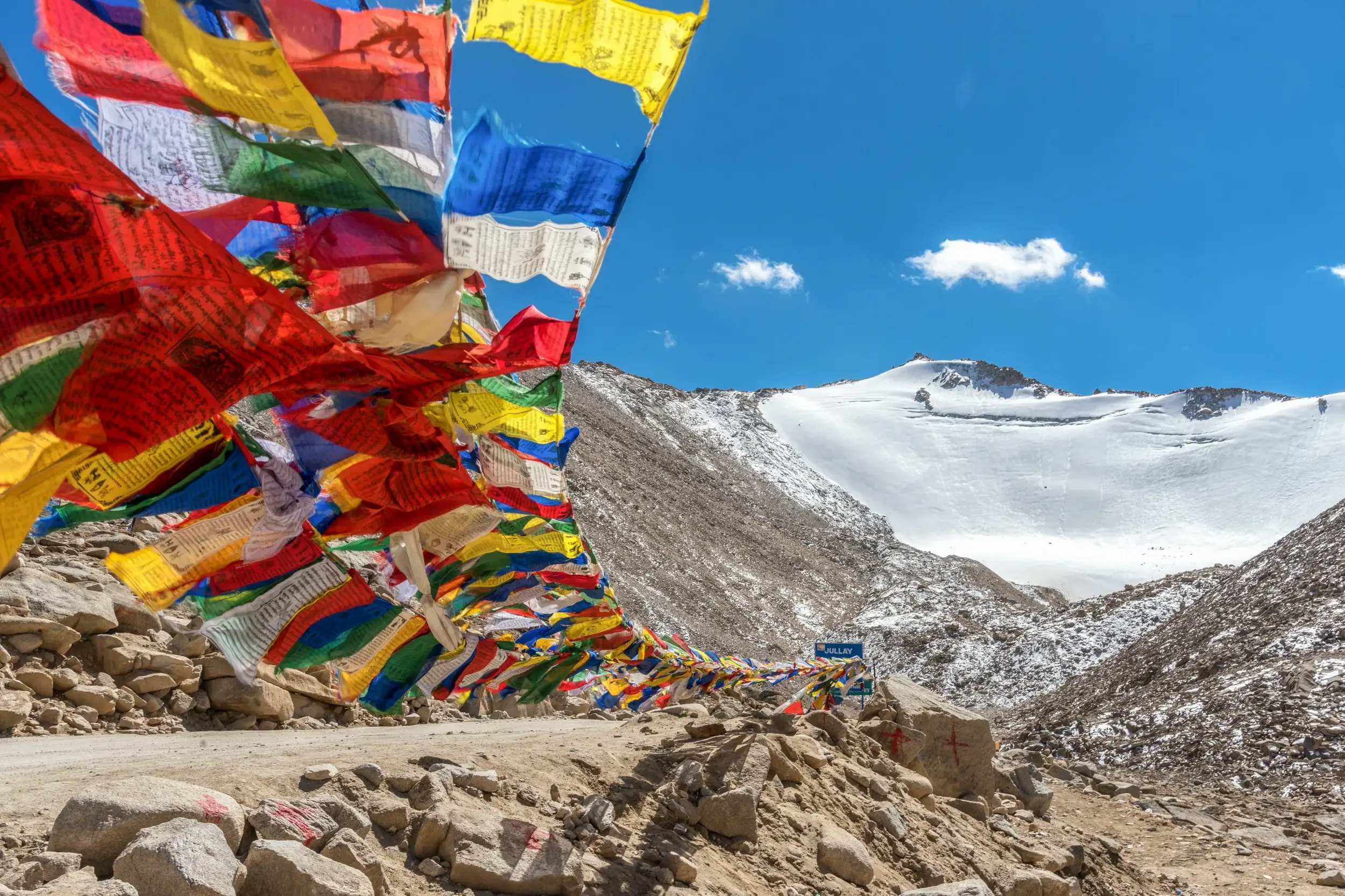 Bunte tibetische Gebetsfahnen wehen im Wind am Khardung La vor einem schneebedeckten Gipfel im Himalaya.